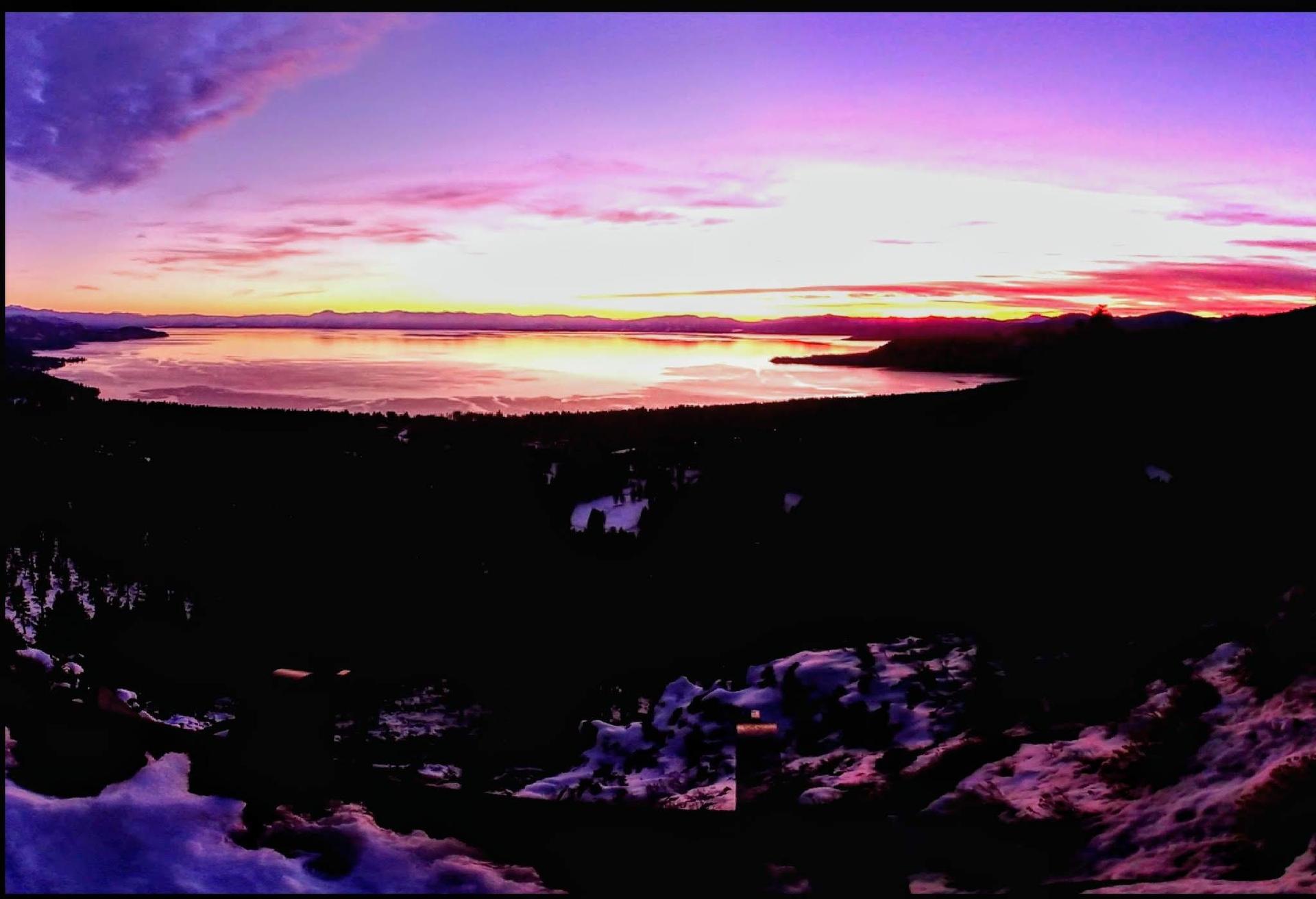 Panoramic view of a lake at sunset with vibrant pink and purple sky.