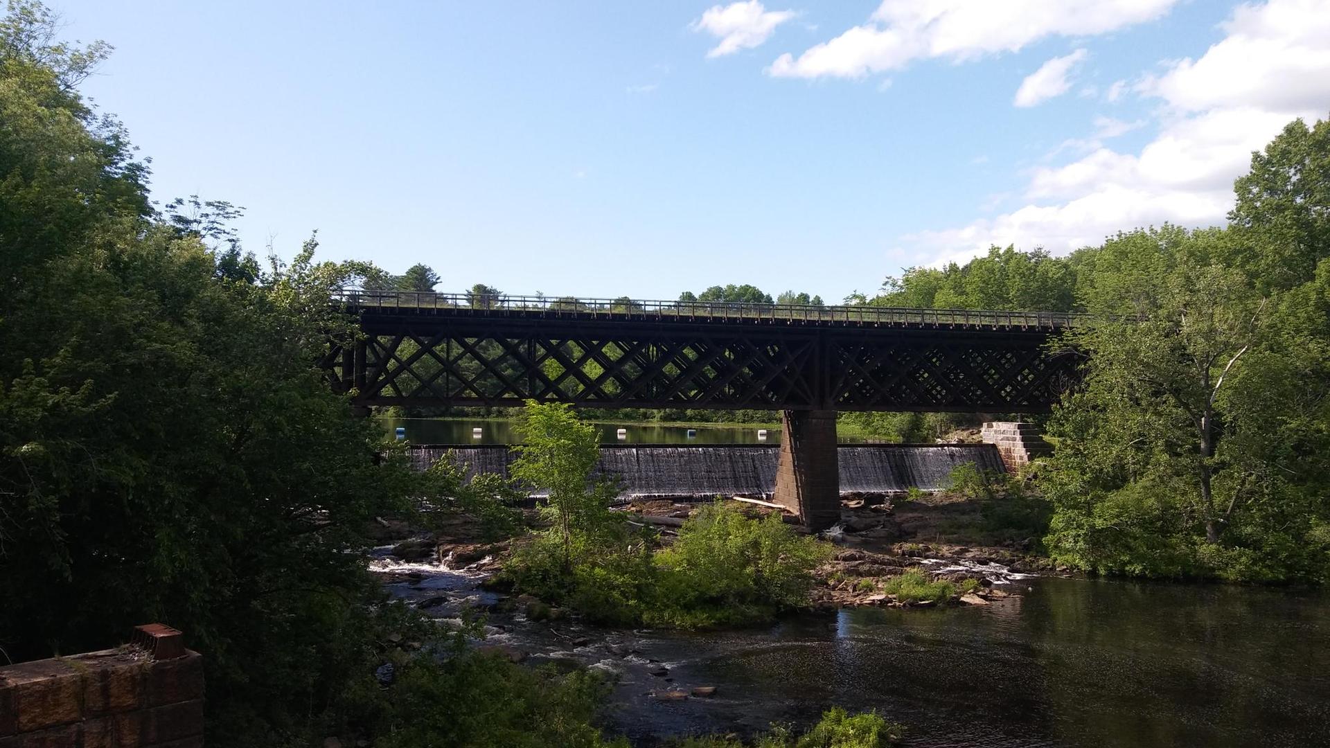 Large metal bridge over a river and dam, surrounded by green trees.
