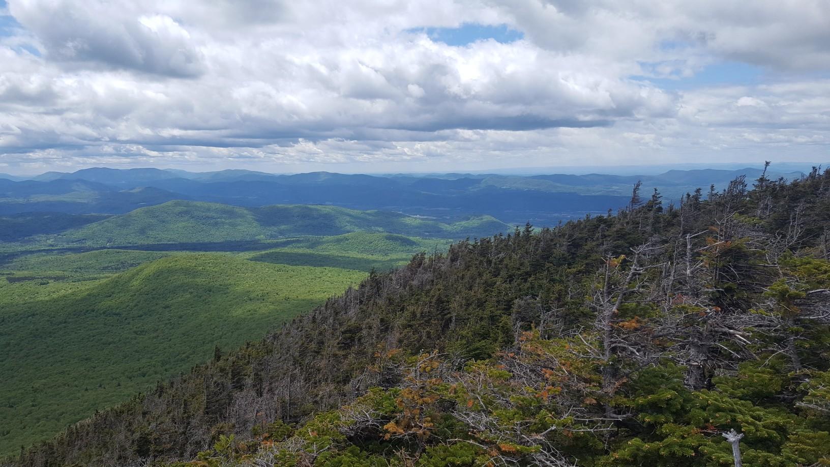 Panoramic view of green forested mountains under a partly cloudy sky.