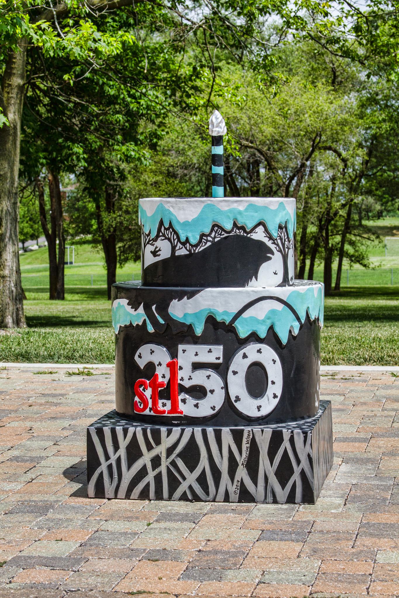 A large, multi-tiered black and teal cake sculpture with '250' outdoors in daylight.