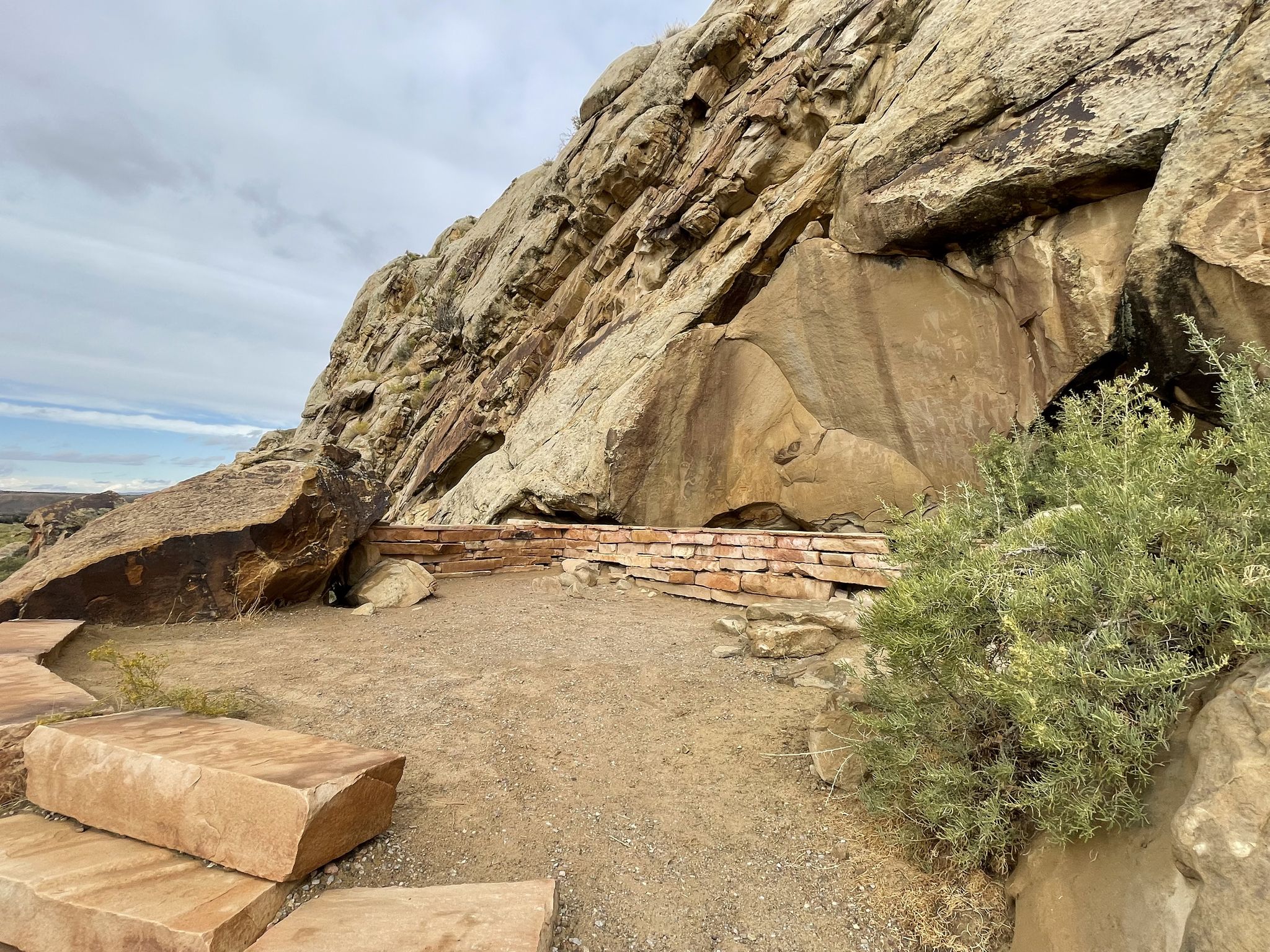 Wide view of a rocky cliff with a stone wall and cut blocks on the ground. - Dinosaur National Monument Scenic Drive