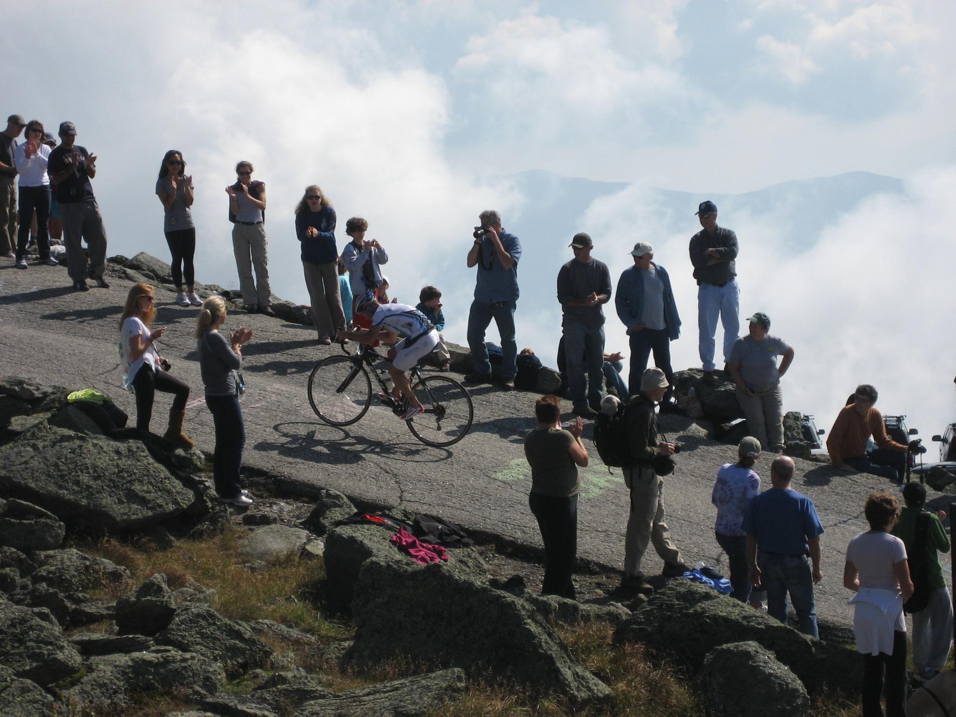 A cyclist rides uphill on a paved road, cheered by spectators.