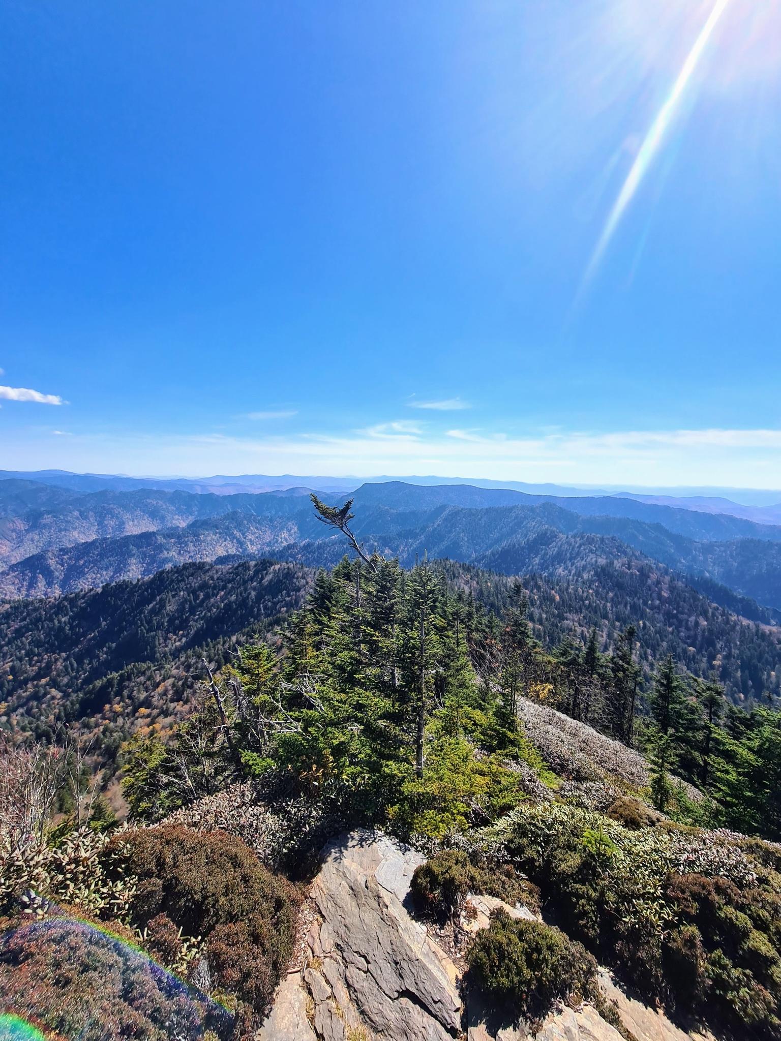 Sunny mountain peak view with distant ranges and a bright sky.