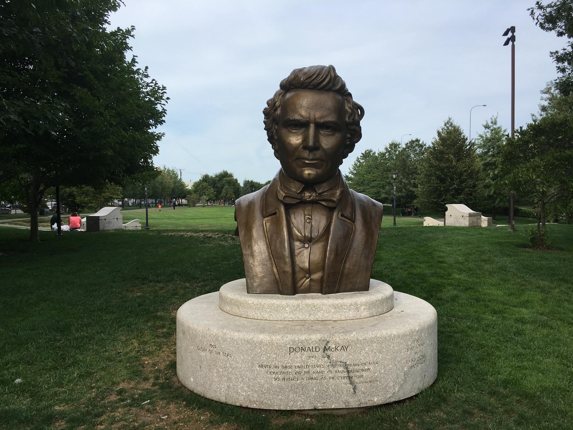 Bronze bust of a man on a pedestal in an overcast park setting.