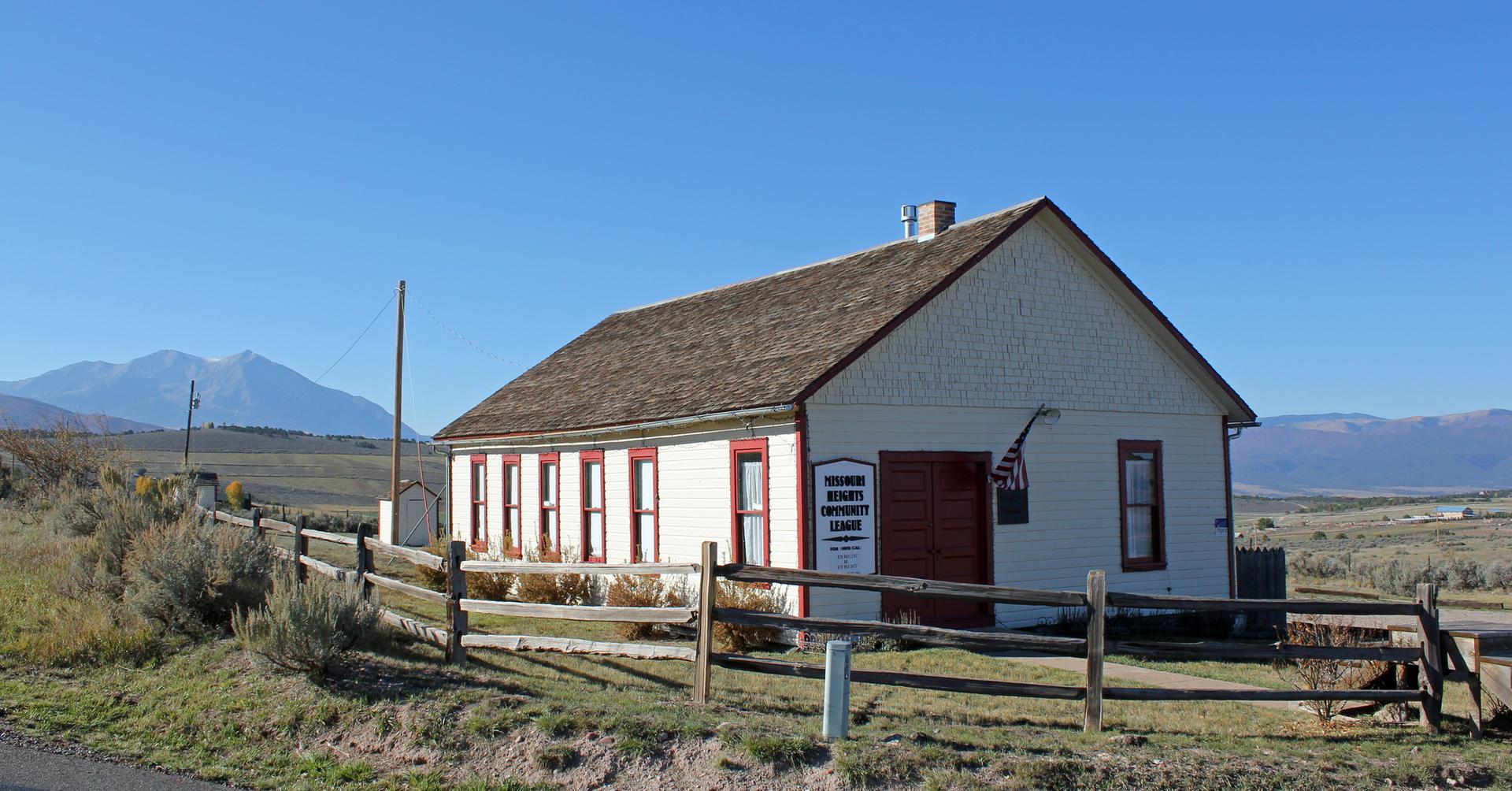 A white building with red trim and a wooden fence under a clear blue sky.