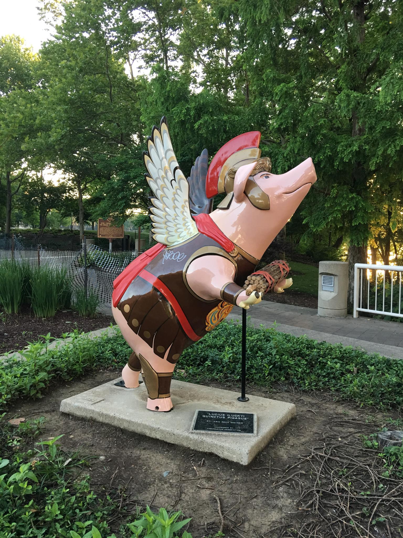 A colorful pig statue with wings and armor stands in a sunny park.