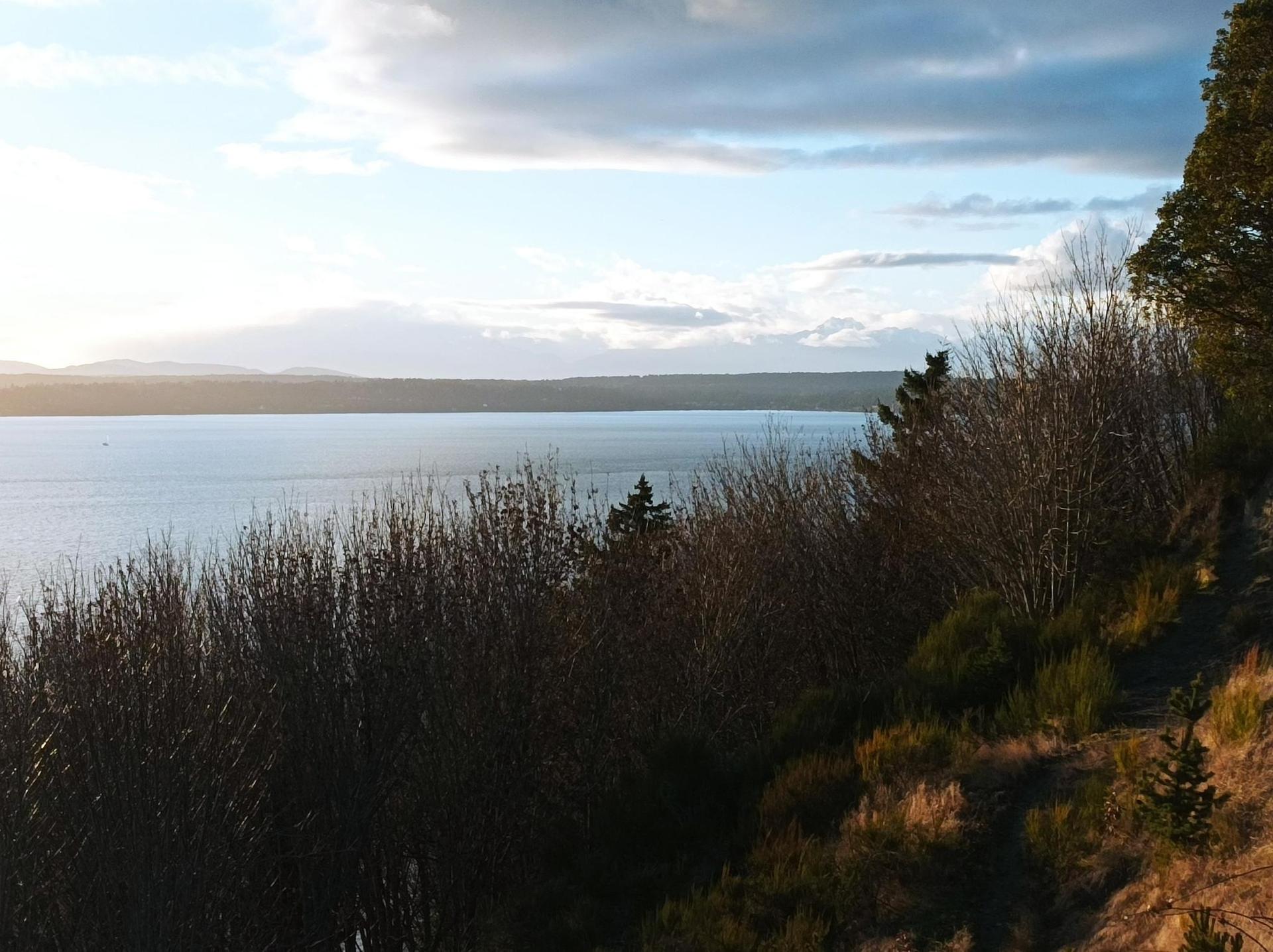 Overcast sky above a large body of water and a dark, forested hillside.
