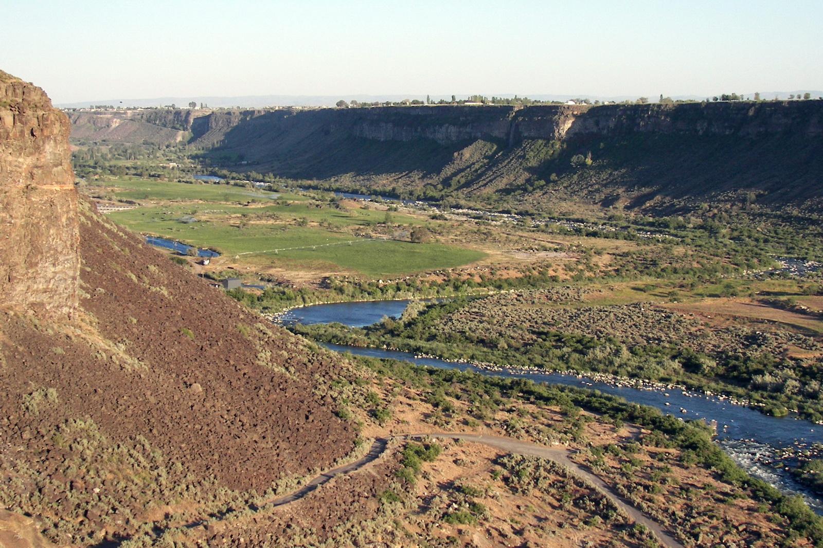 River flows through a wide canyon with green fields and arid slopes in daylight.