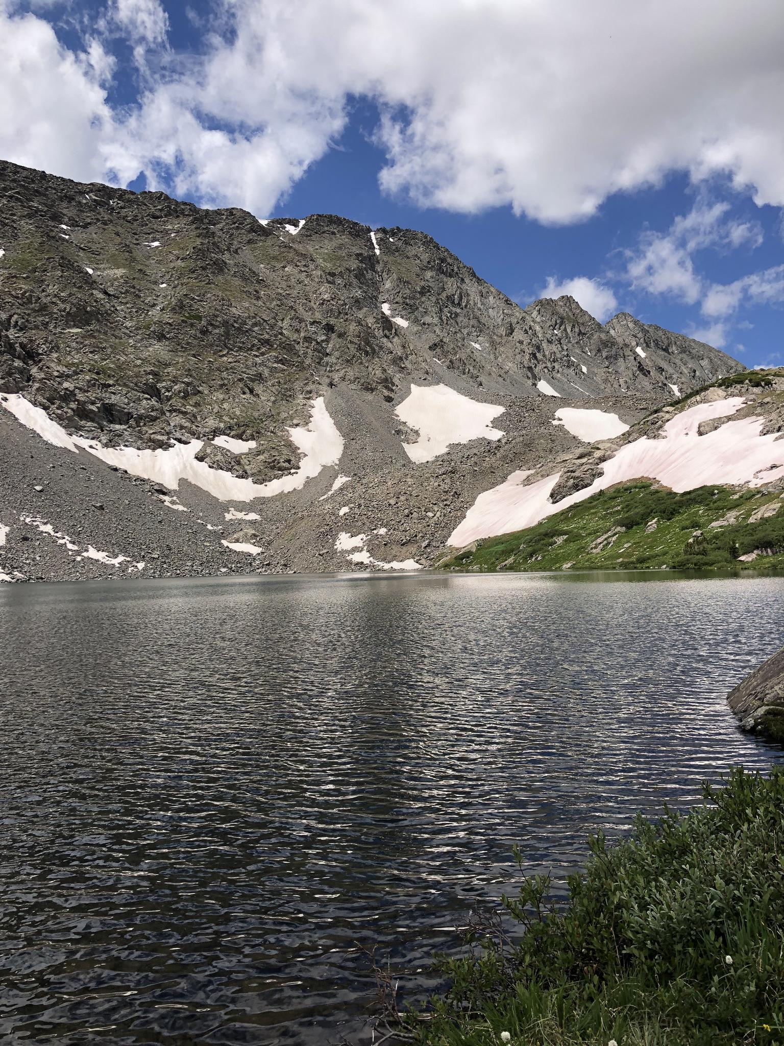 Expansive mountain lake with snow-dusted rocky peaks under a blue sky.