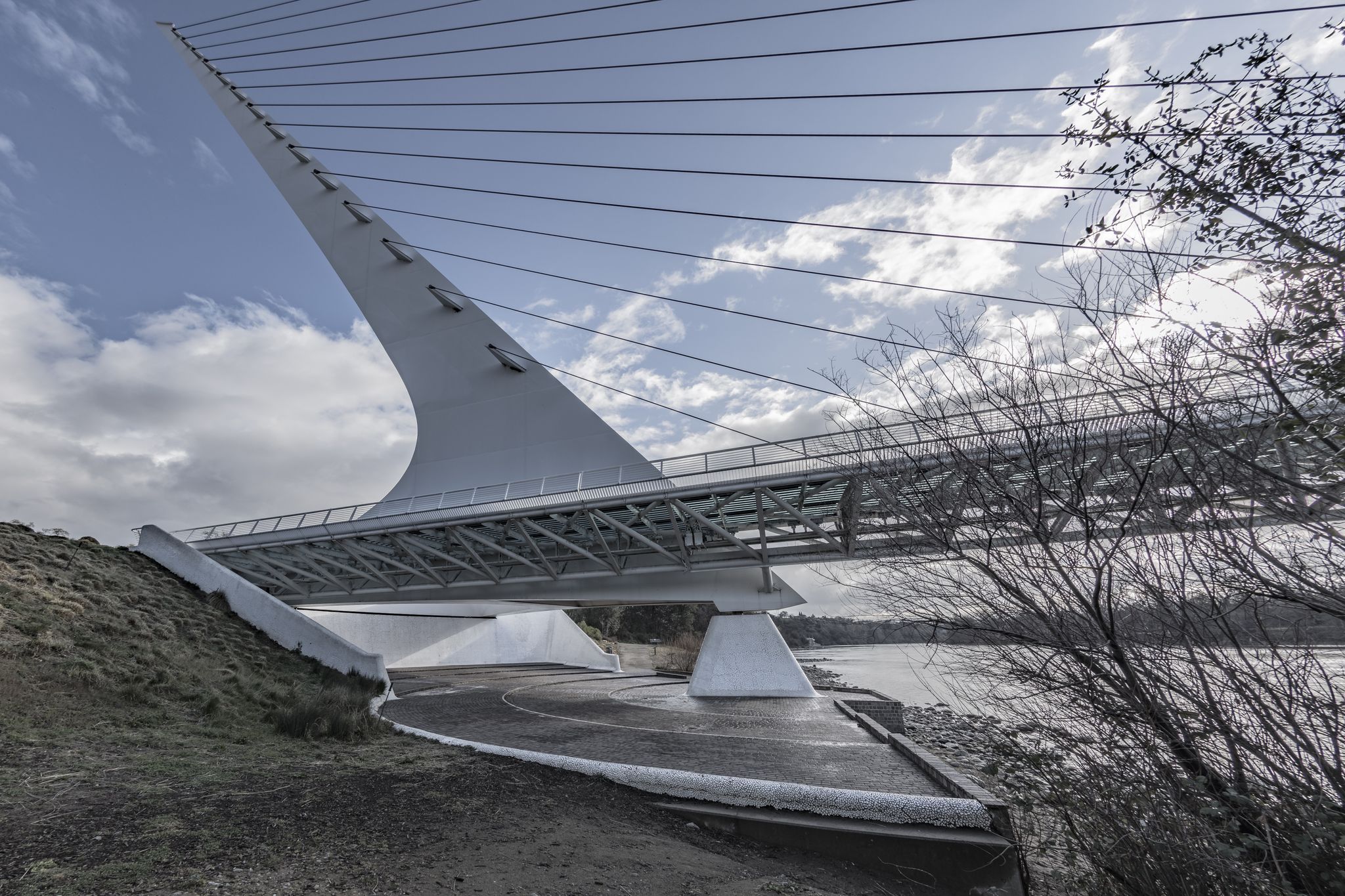 Modern white cable-stayed bridge spanning over water under a cloudy sky. - Sundial Bridge – Ribbon Bridge loop from S. Bonnyview Rd at E. Bonnyview Rd