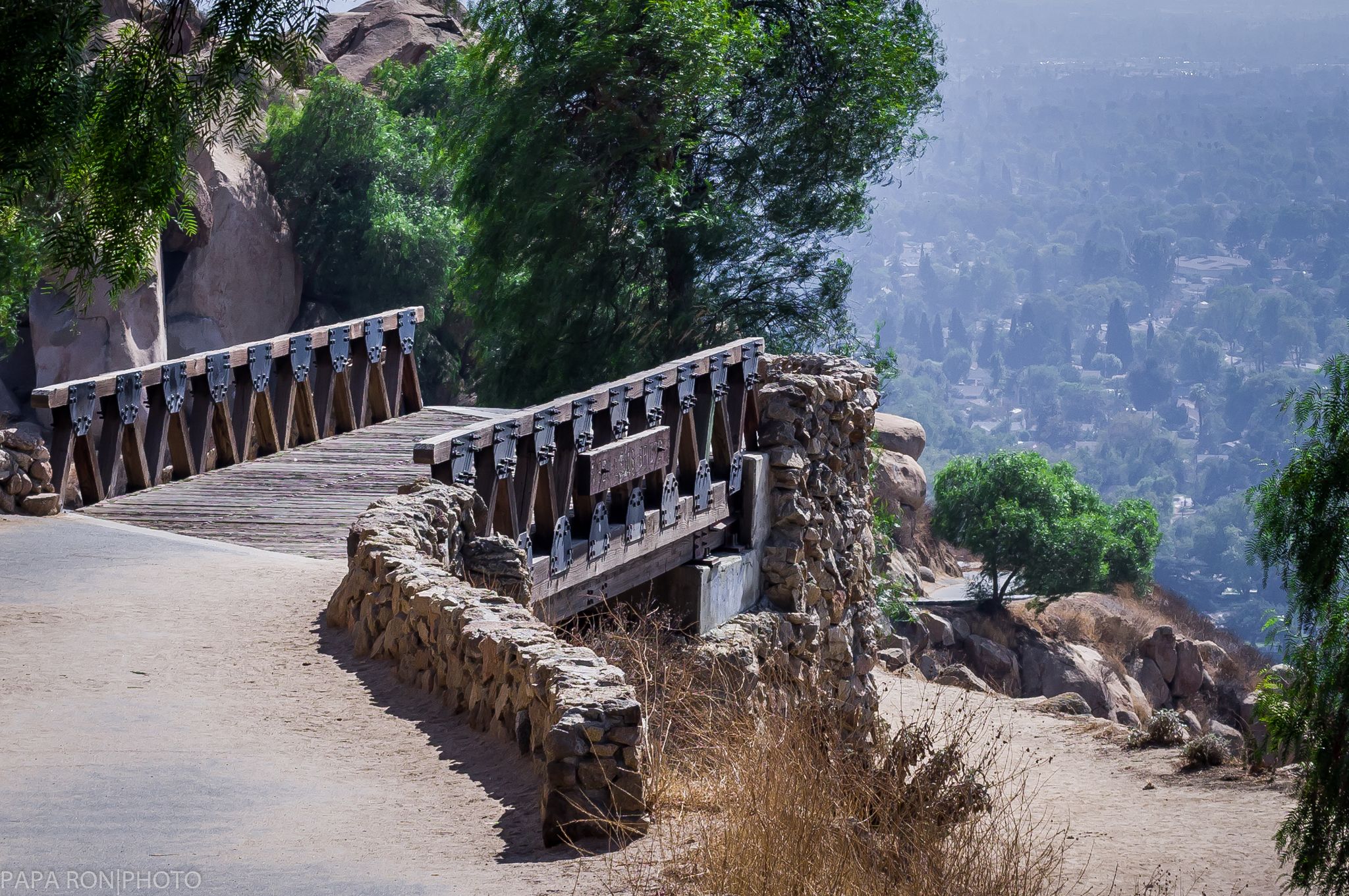 A rustic wooden bridge with stone walls extends over a hazy valley. - Mount Rubidoux loop from Riverside