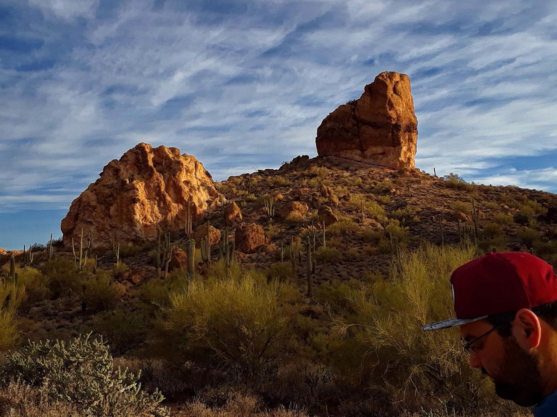 Person in red cap observing large desert rock formations and cacti.