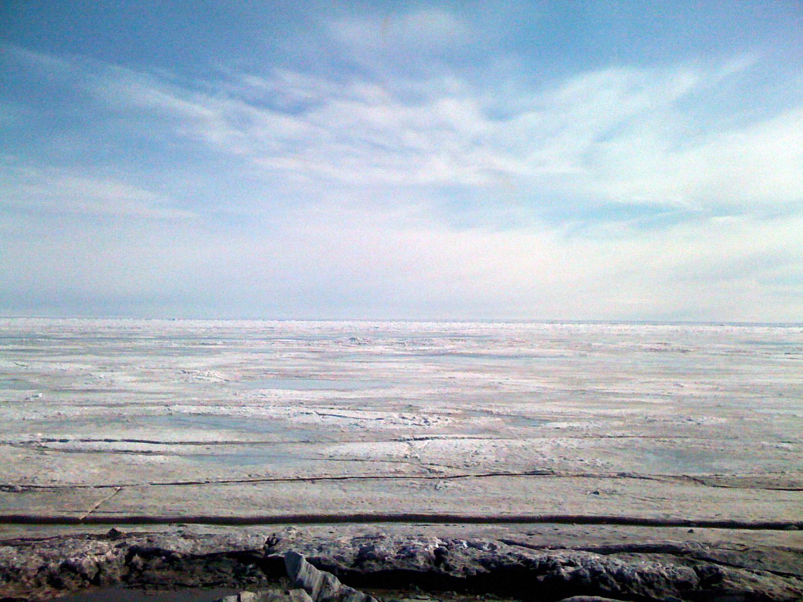 Vast, flat expanse of ice under a bright, cloudy sky.
