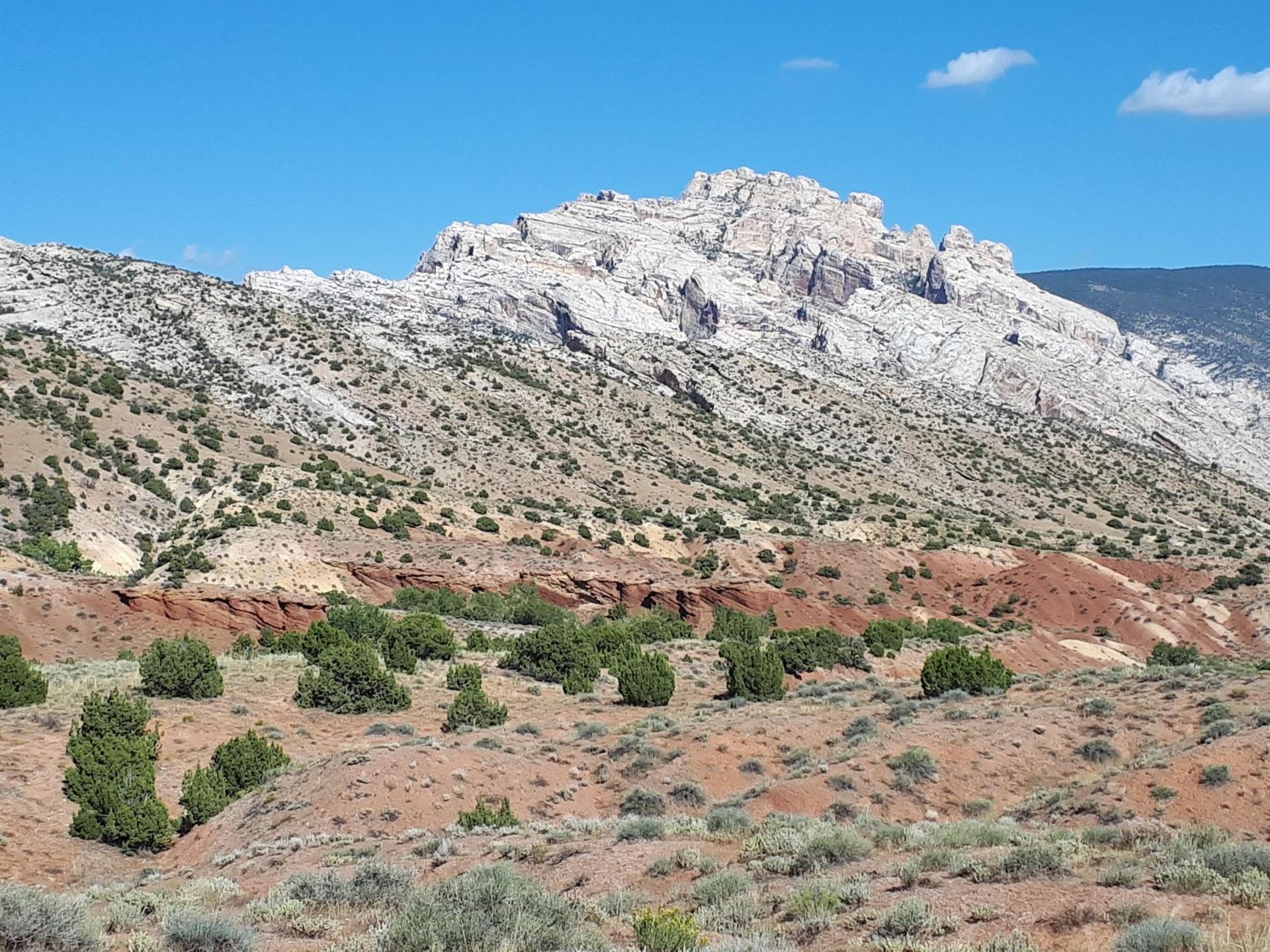 Vast desert landscape with a large white mountain and red hills under a blue sky.