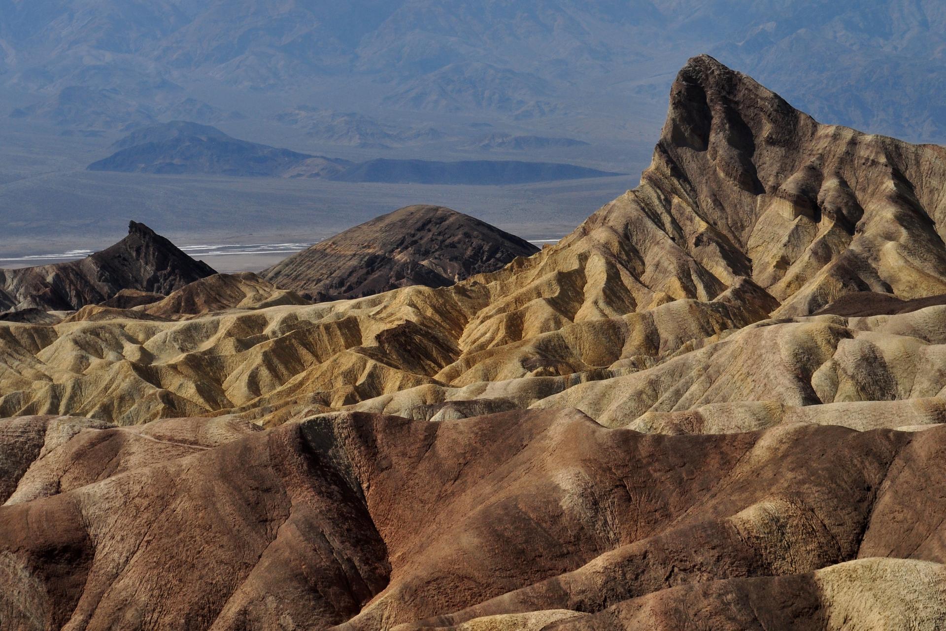 Rugged, eroded desert mountains with varied colors under a hazy sky.