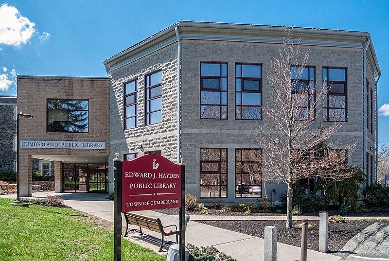A modern stone building with large windows, a sign, and a bench.