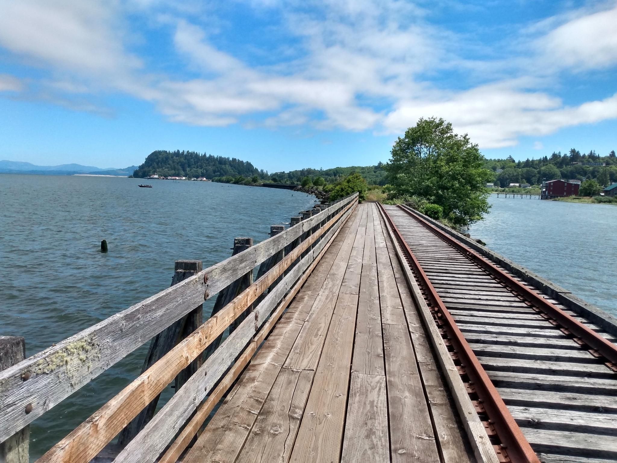 Wooden bridge with railroad tracks and a walkway over water on a sunny day. - Astoria Riverwalk Loop