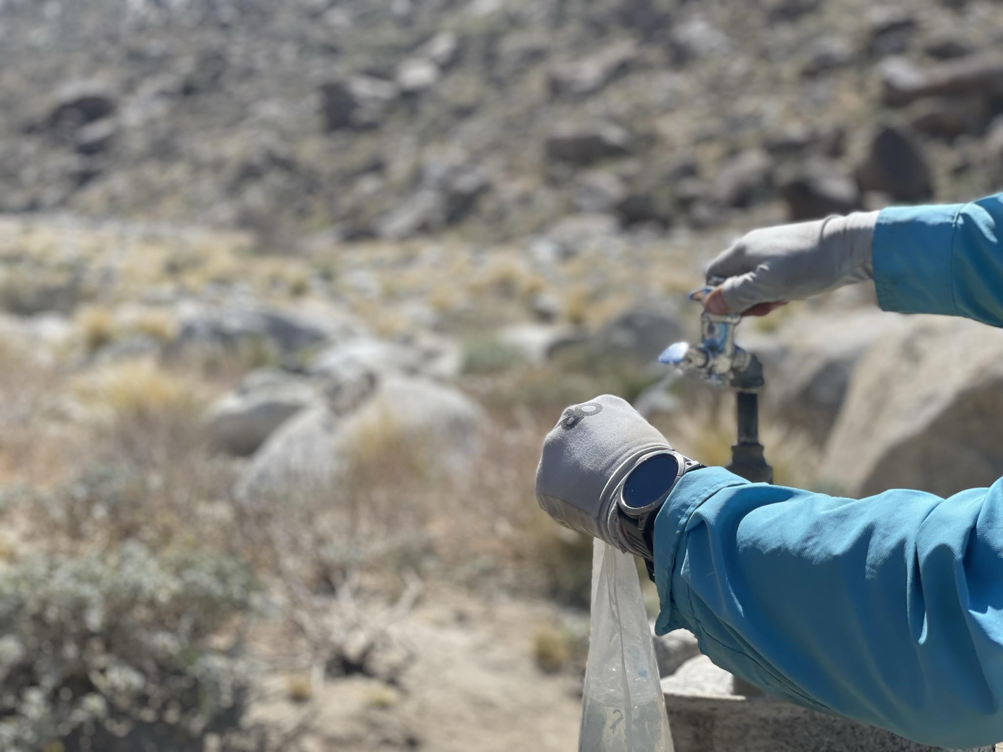 Person in gloves filling a bag with water from an outdoor spigot.