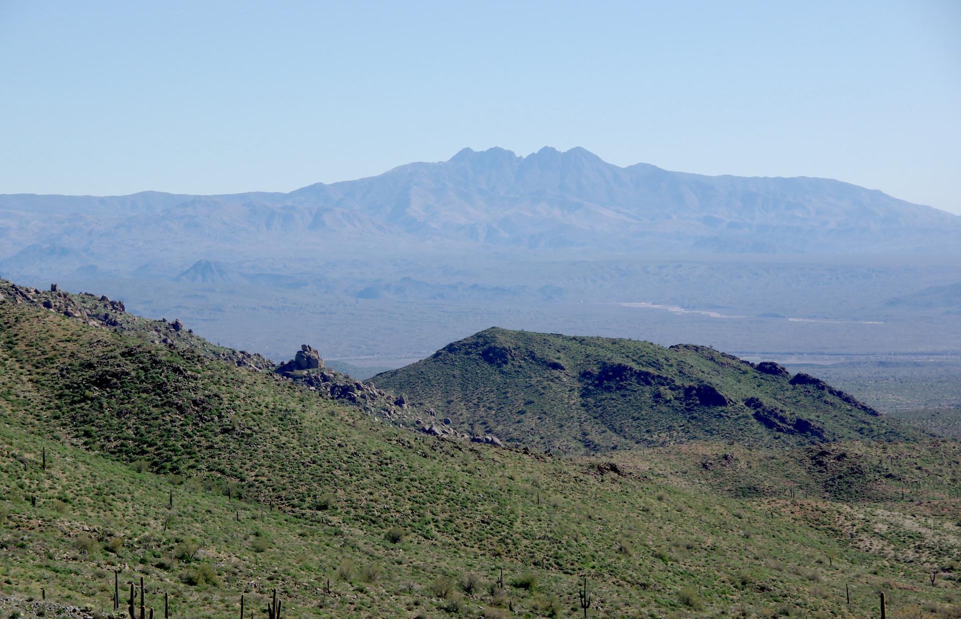 Sunny desert view with green, rocky hills and distant, hazy blue mountains.