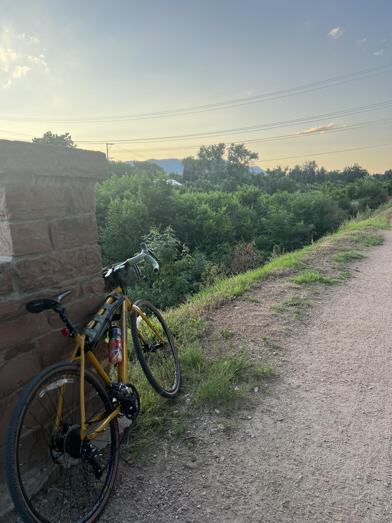 Yellow bicycle leaning on a stone wall beside a dirt path at sunset.
