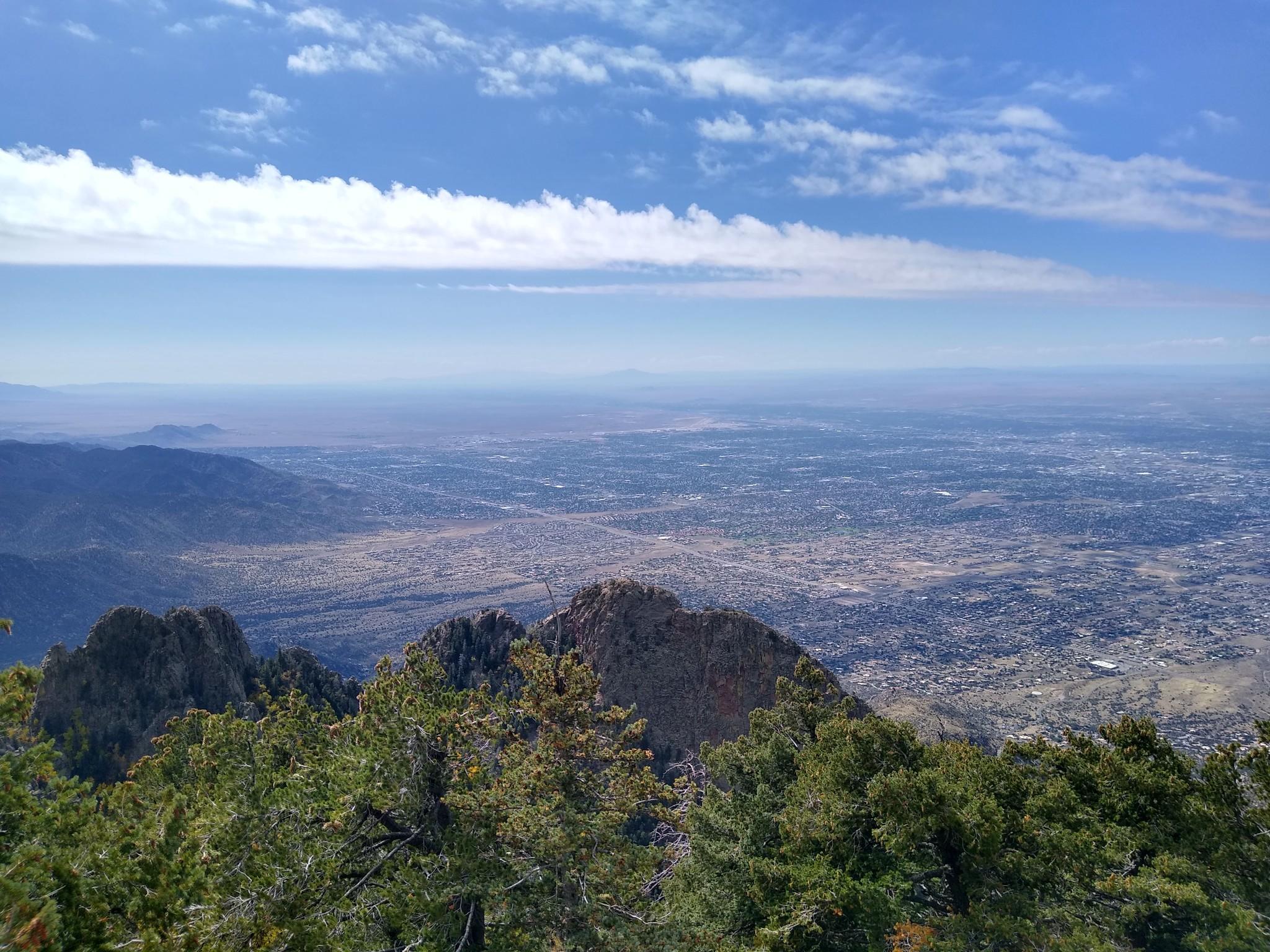 Bright day over mountain peaks, dense forest, and a sprawling valley below.