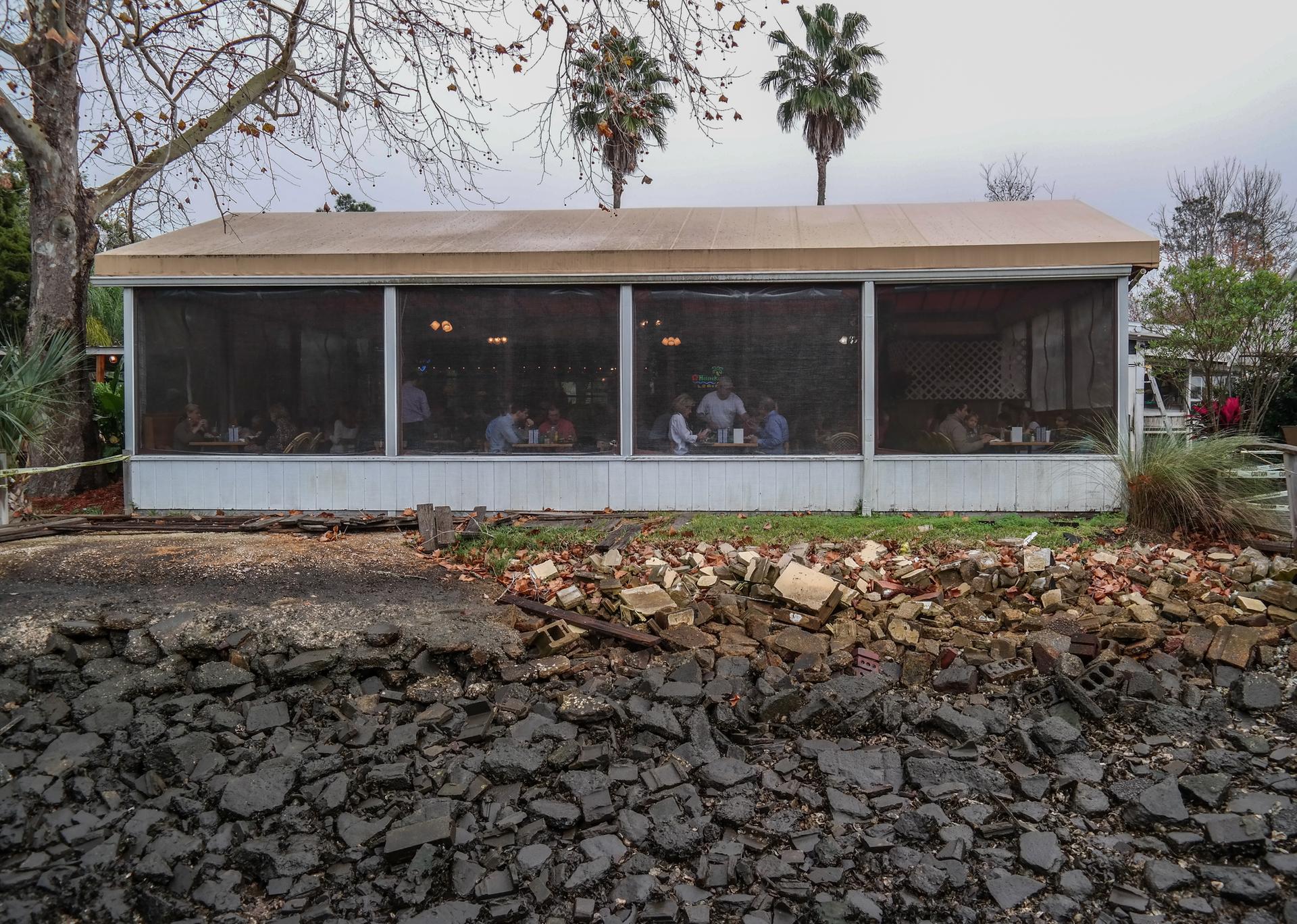 People dining inside a screened building with trees and debris outside.