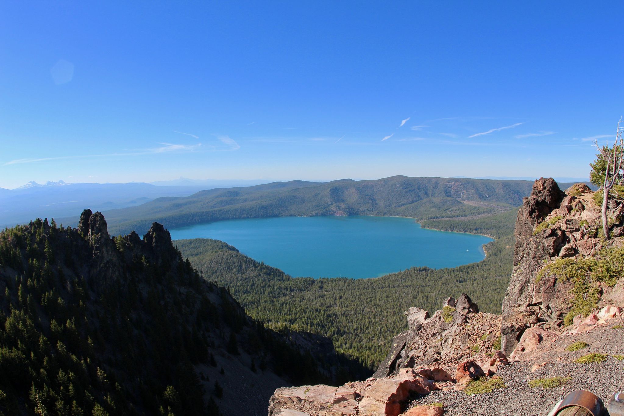 Vibrant blue lake surrounded by green forests and rocky mountains. - Paulina Peak Trail