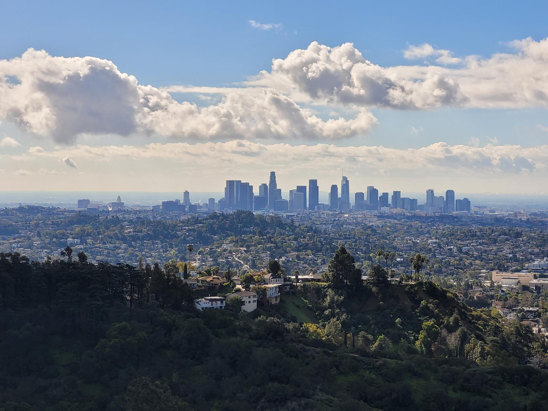 Distant city skyline under a bright blue sky with fluffy white clouds.