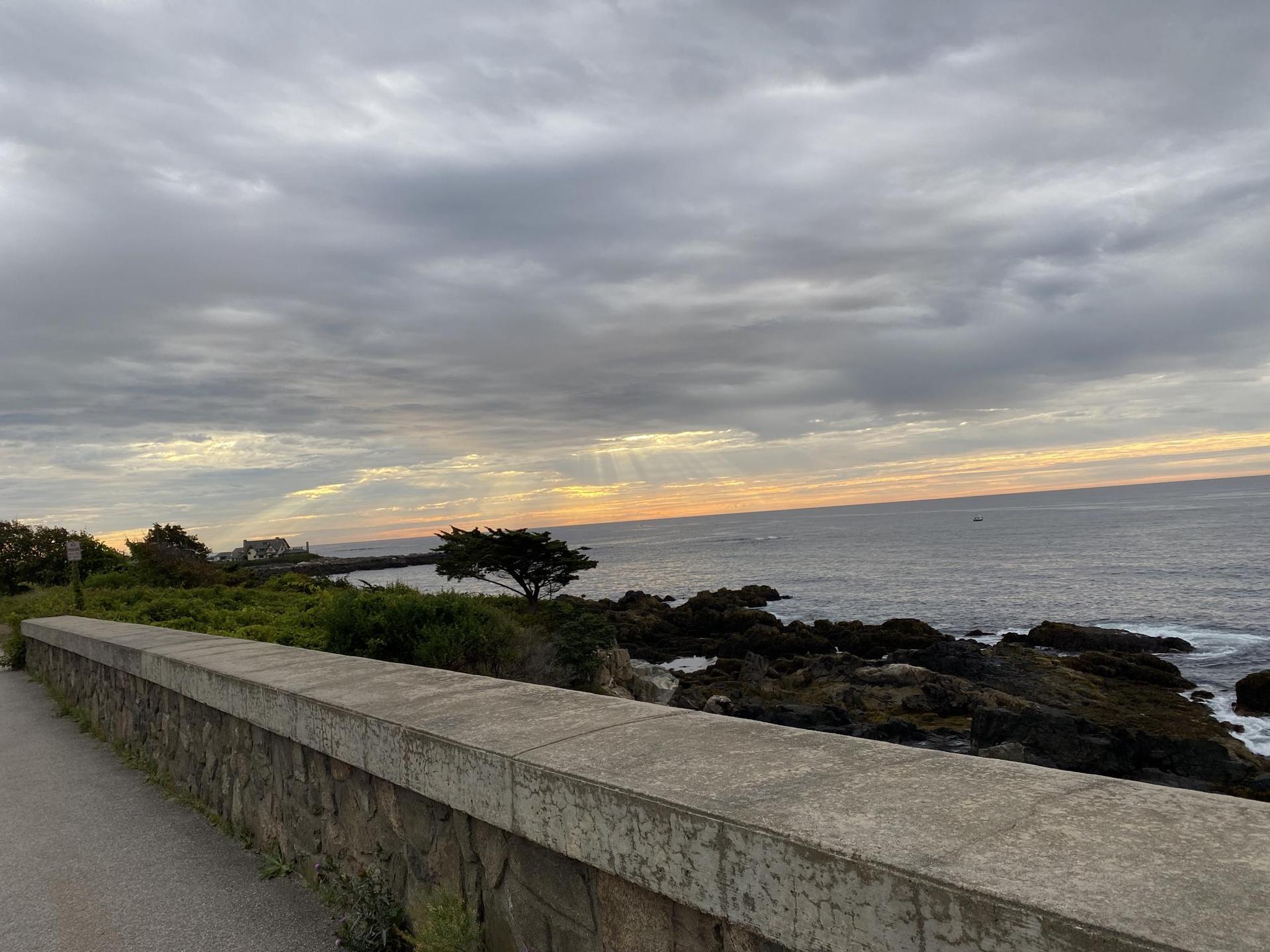 Cloudy sunset over a rocky coastline, viewed from a stone wall.