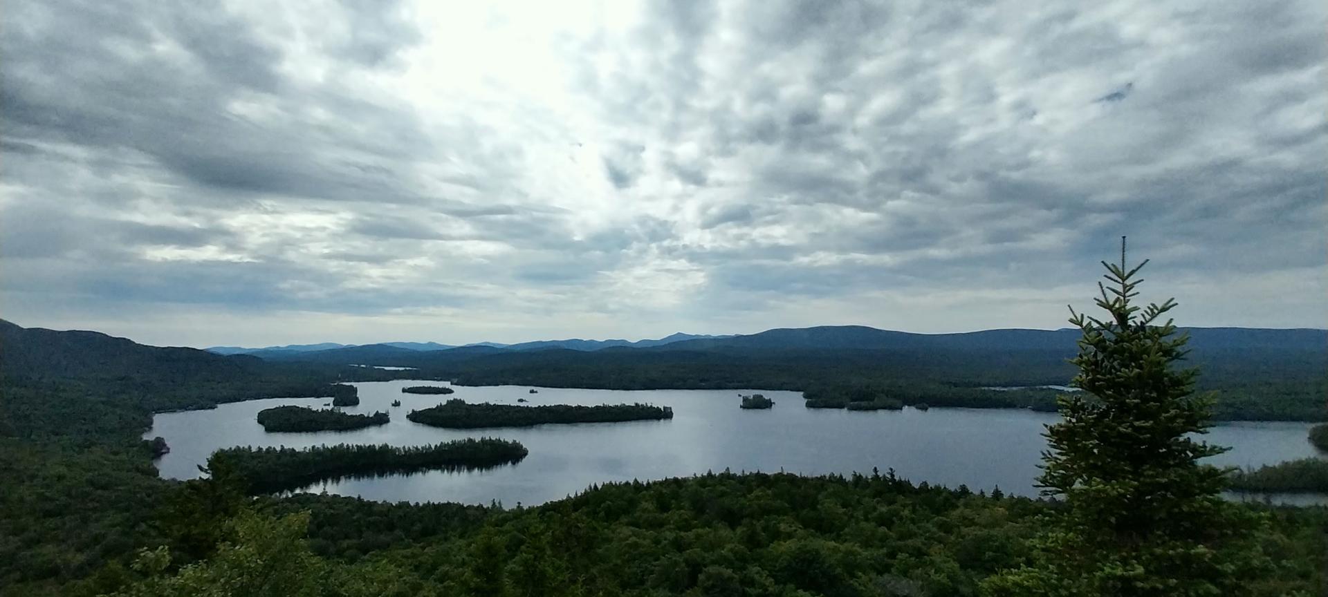Overcast view of a vast lake with islands, surrounded by dark green forests.