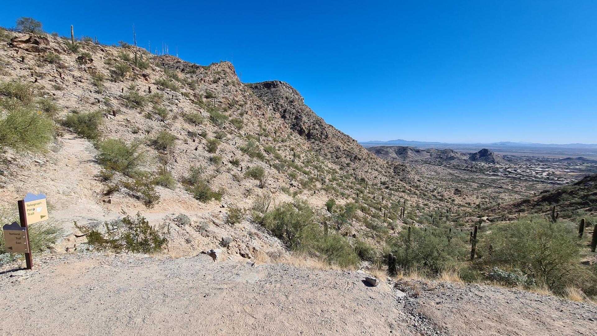 Rocky desert hillside with sparse vegetation overlooking a distant city.