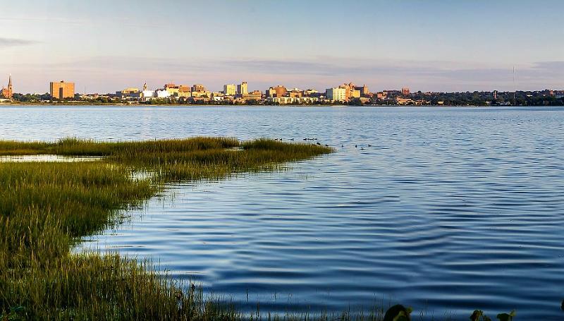 City skyline across calm water with marsh grass in soft light.