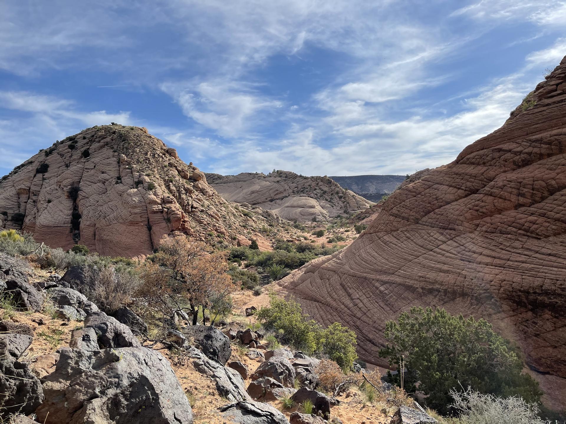 Unique striped rock formations and desert hills under a bright, cloudy sky.