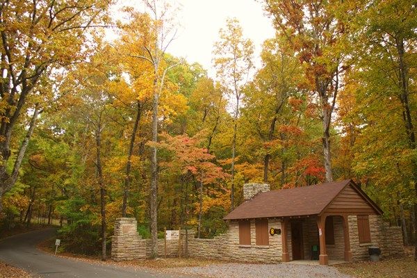 Small building with stone walls and brown roof amidst colorful autumn trees. - CCC Museum loop from Desoto State Park
