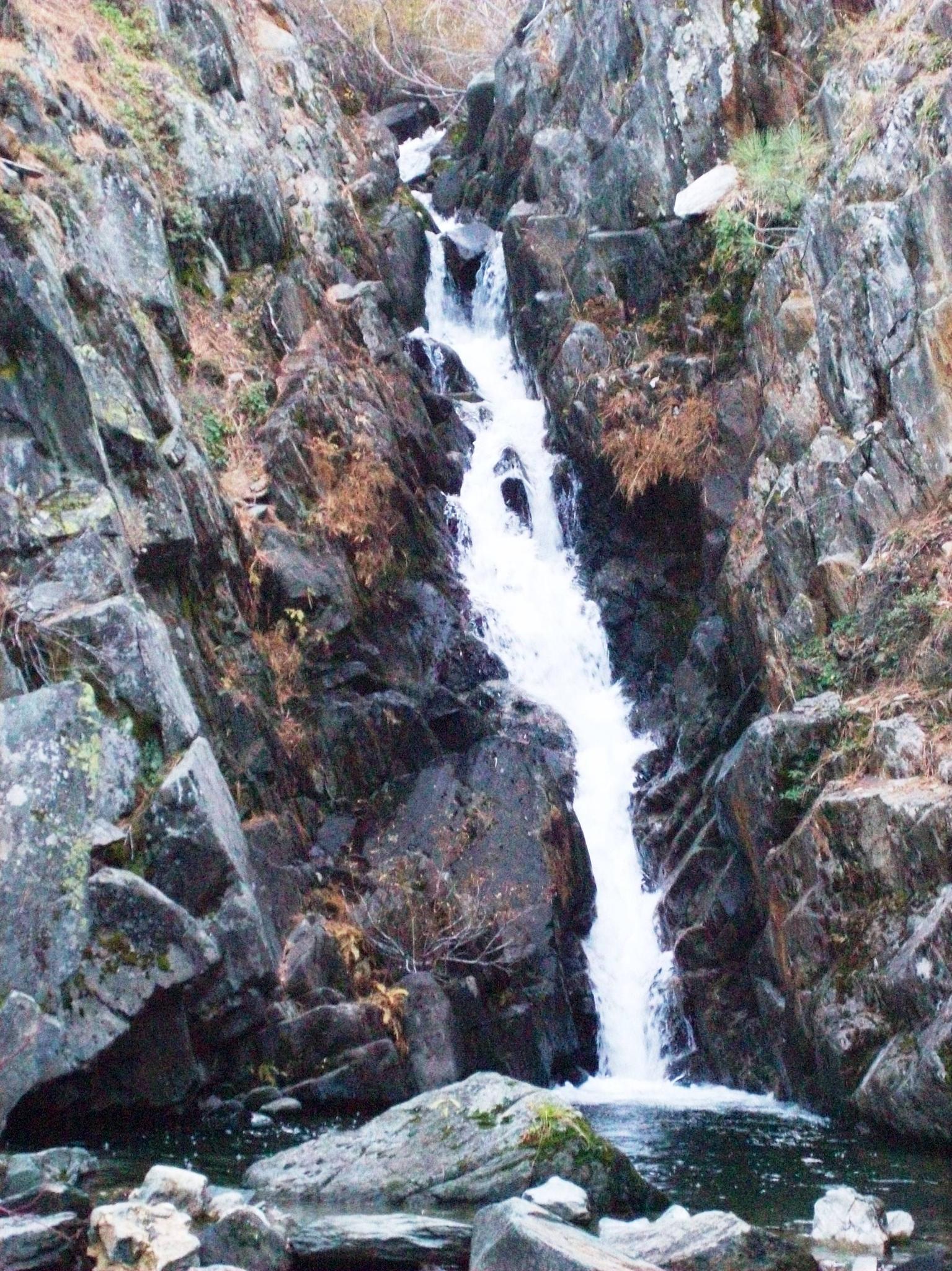 White waterfall cascades down a dark, rocky gorge into a pool.