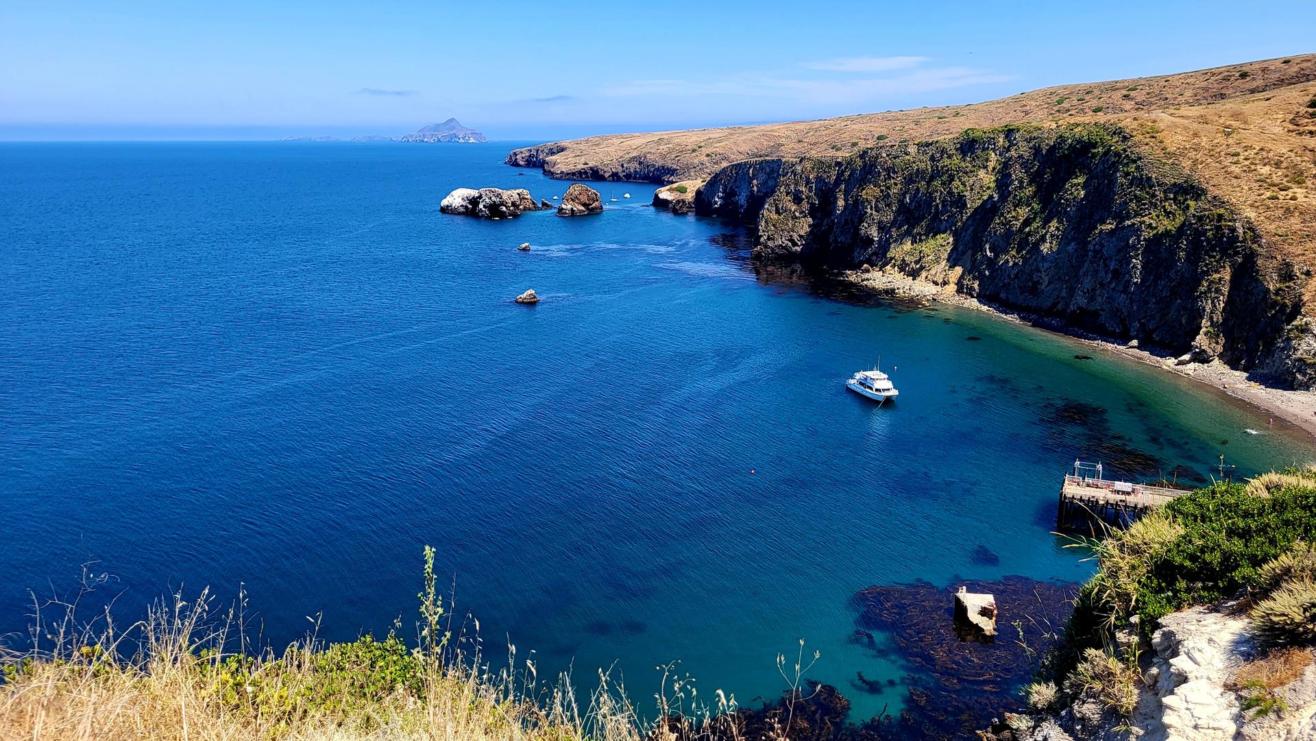 Bright blue ocean and rocky coastline with a boat in a sunny bay.