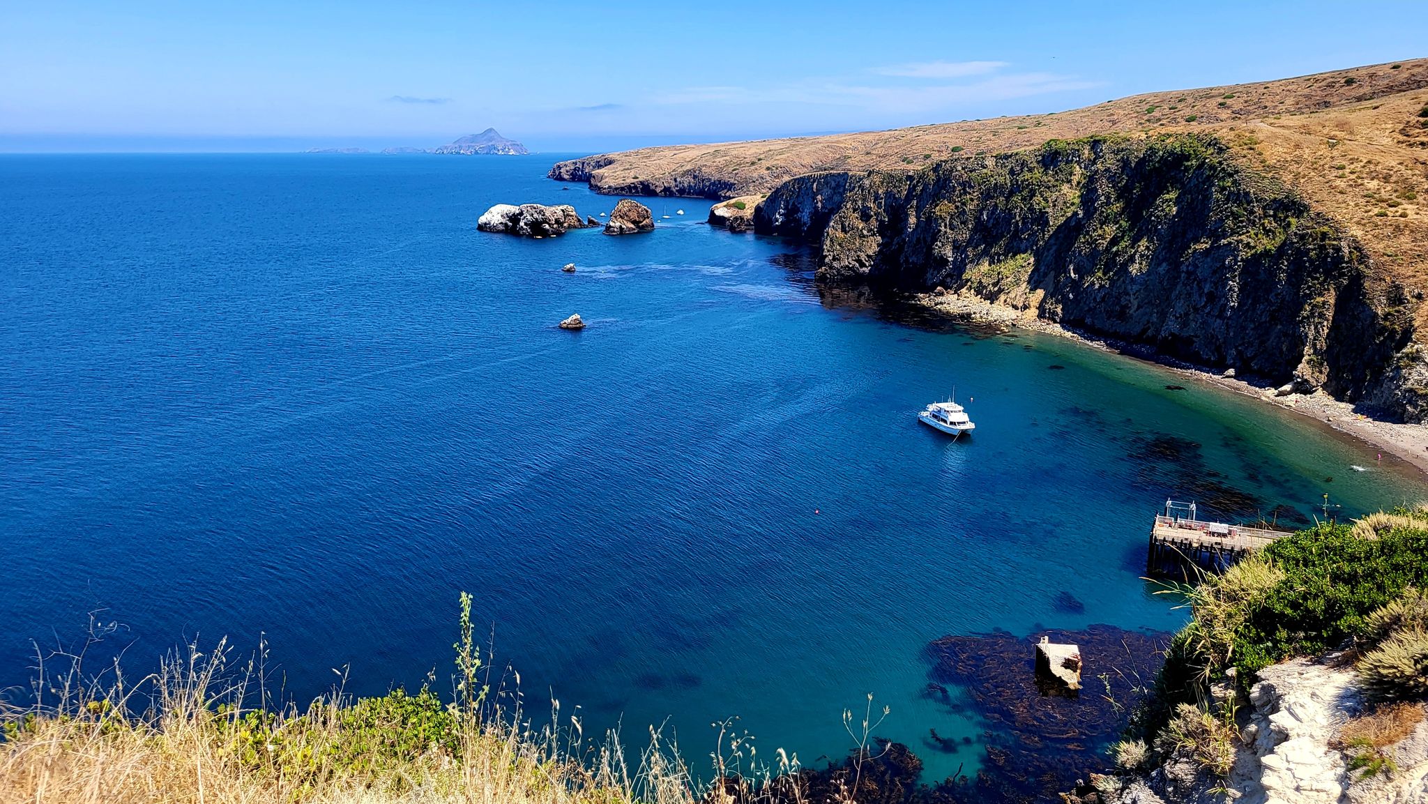 Bright blue ocean and rocky coastline with a boat in a sunny bay. - Montañon Ridge Loop