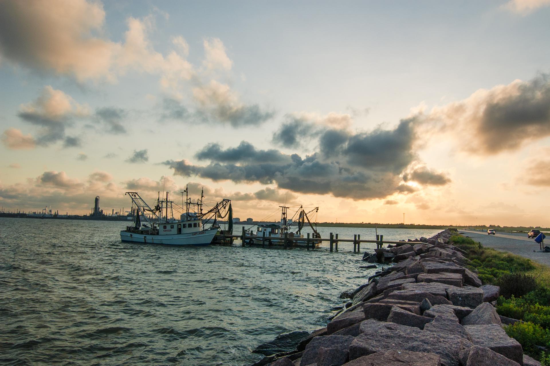 Fishing boats docked at a pier during a warm, cloudy sunset.
