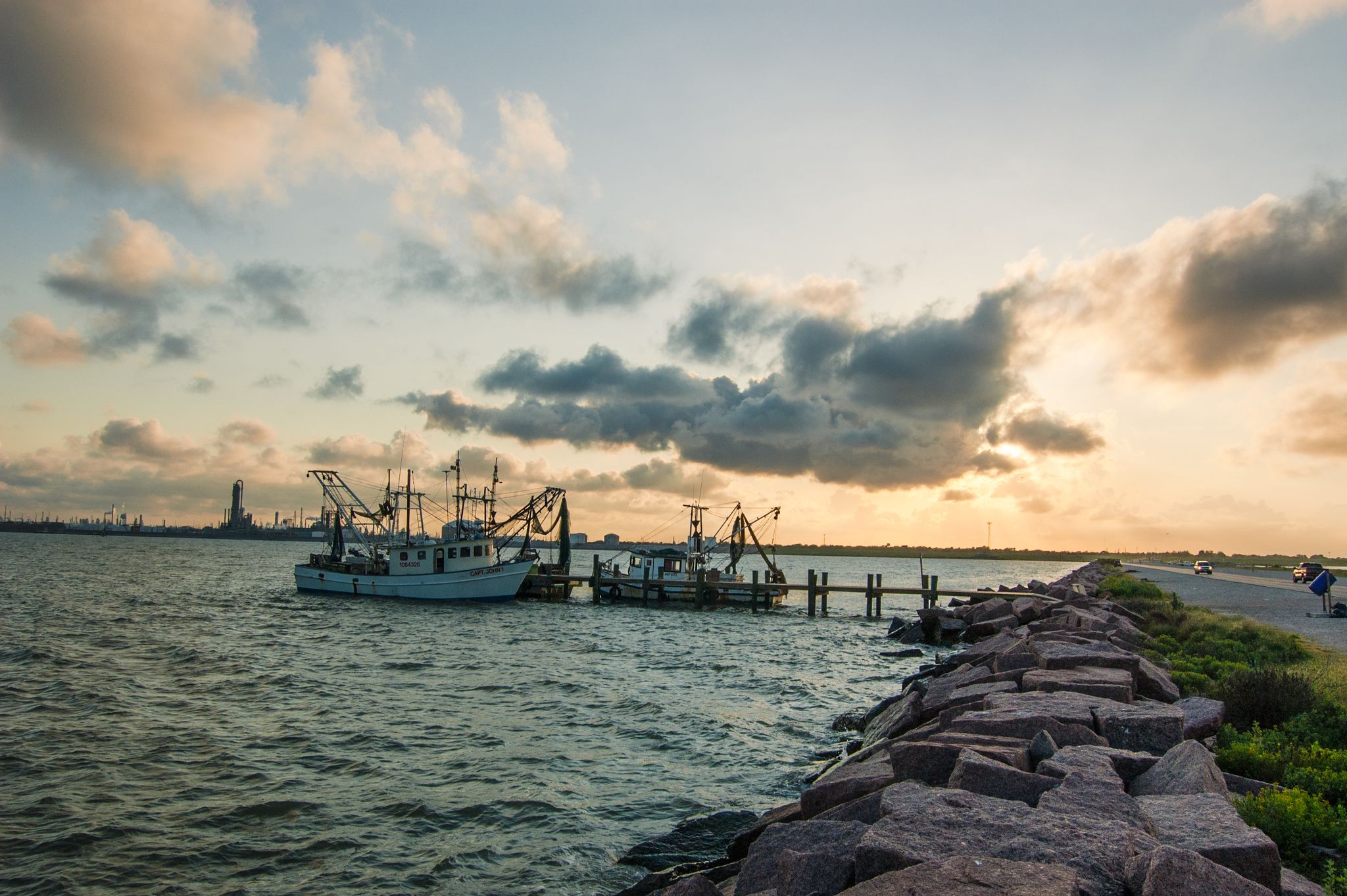 Fishing boats docked at a pier during a warm, cloudy sunset. - Texas City Dike Trail
