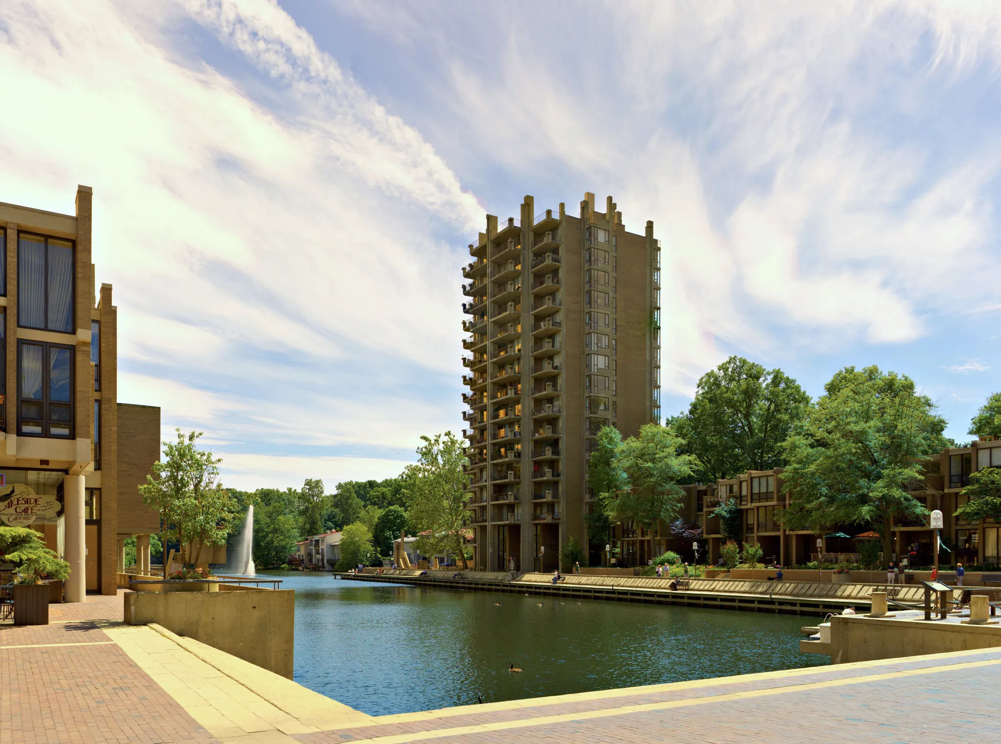 Modern buildings and a tall tower overlook a canal with a fountain on a sunny day. - Lake Anne Plaza – Bridge to W&OD Trail Access loop from Great Falls Crossing