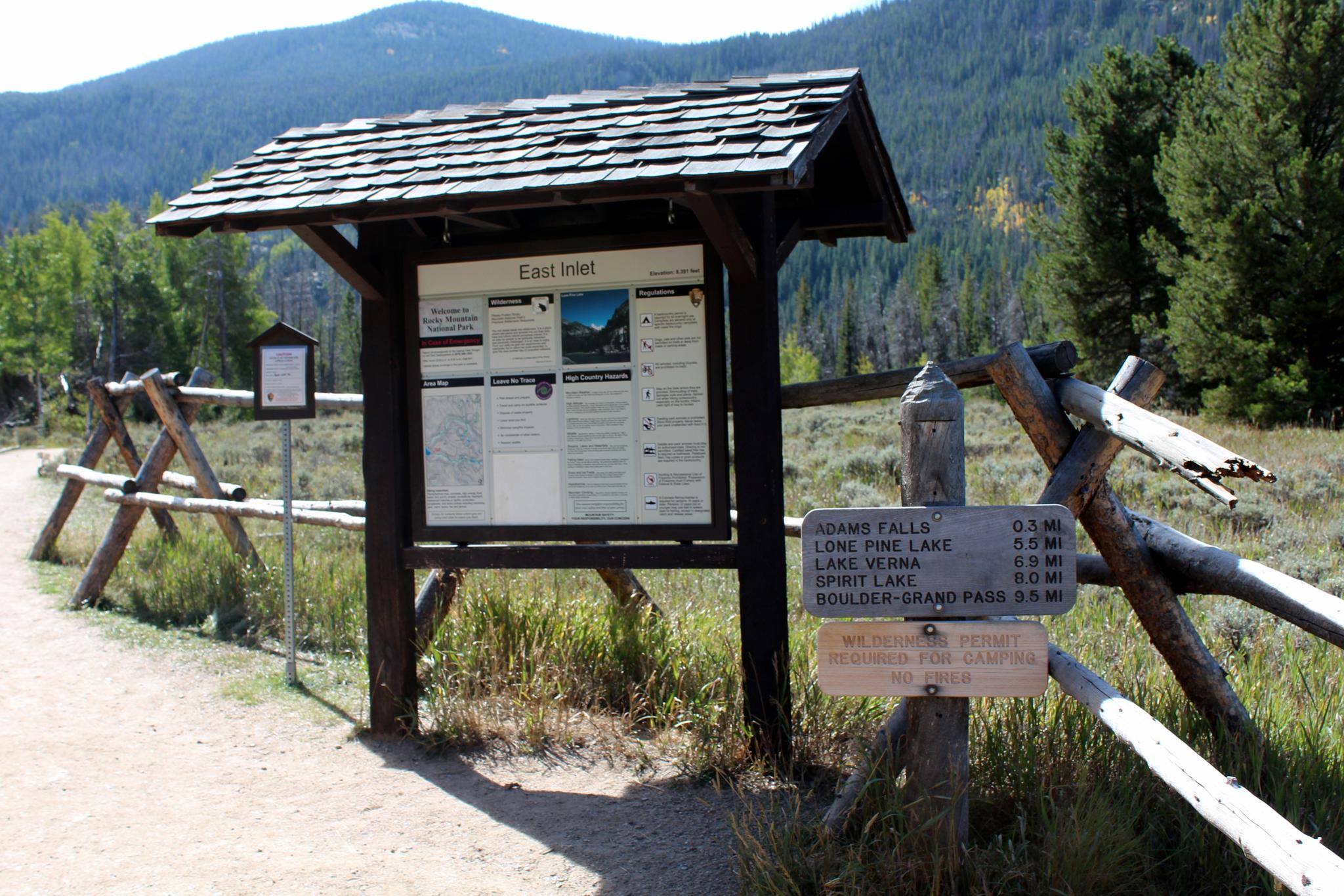 Wooden trail sign and information board next to a split rail fence.
