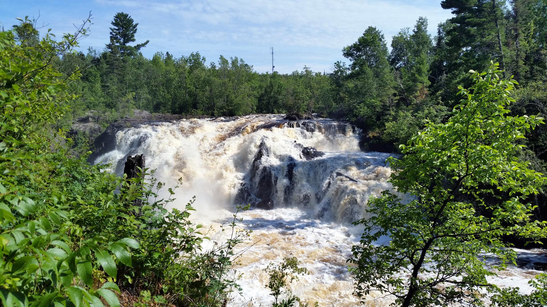 Powerful waterfall in a rocky river, surrounded by dense green forest.