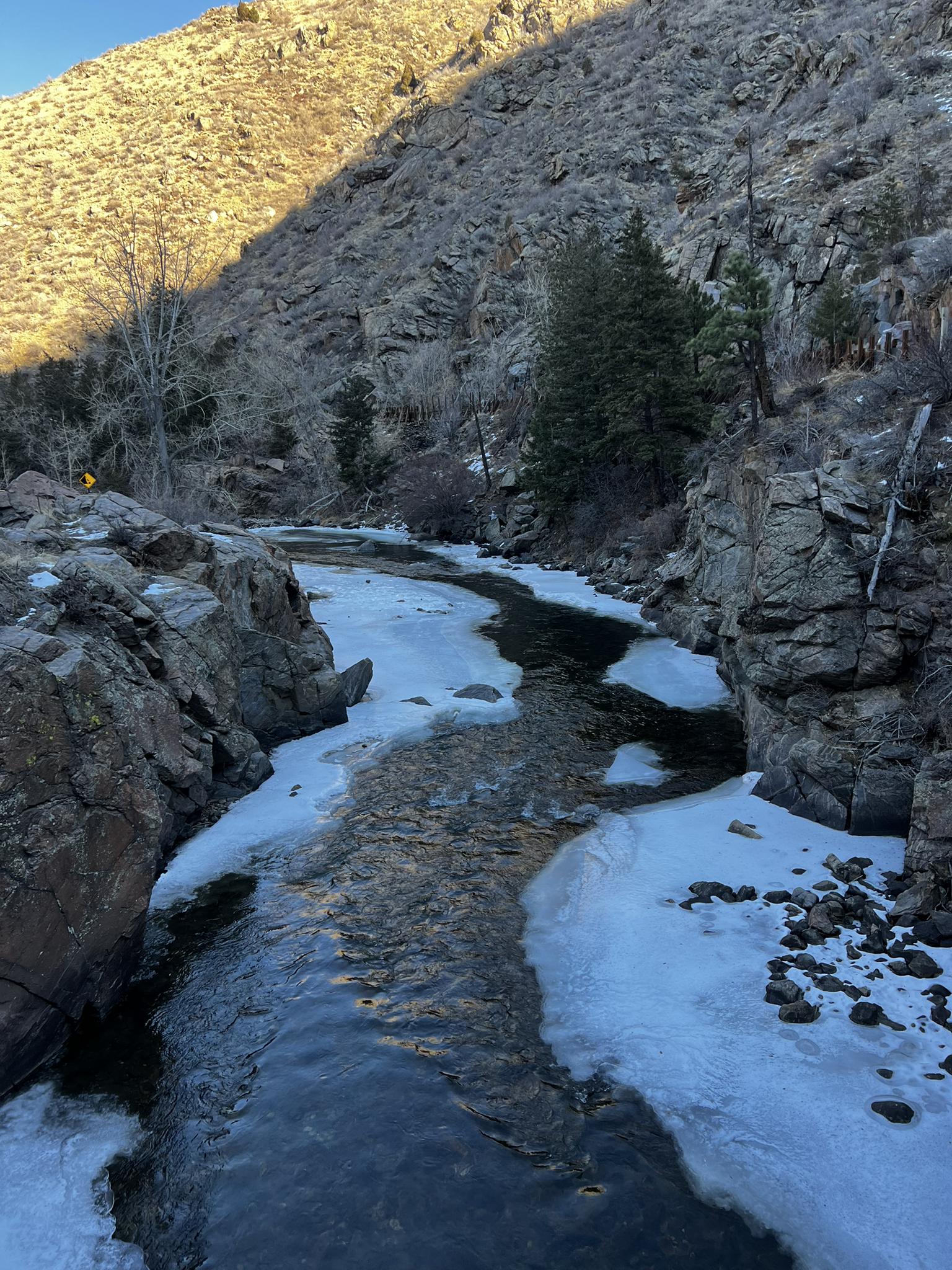 Icy river flowing through a rocky canyon with a sunlit mountain slope.
