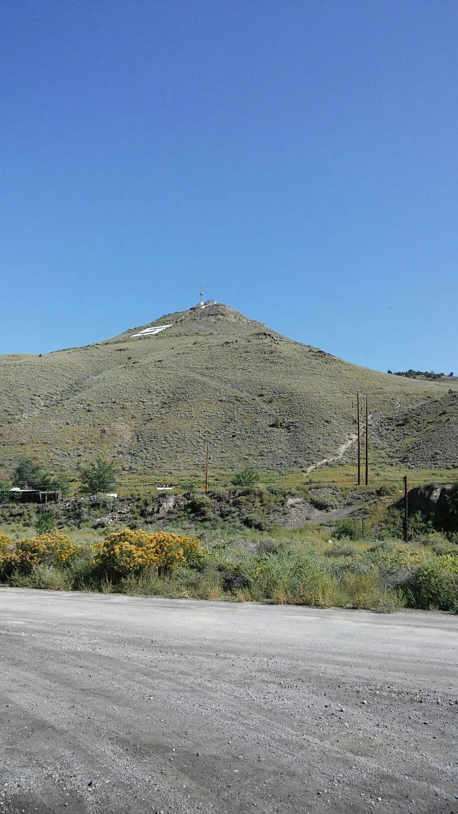A large, barren hill under a clear blue sky, with a dirt road.