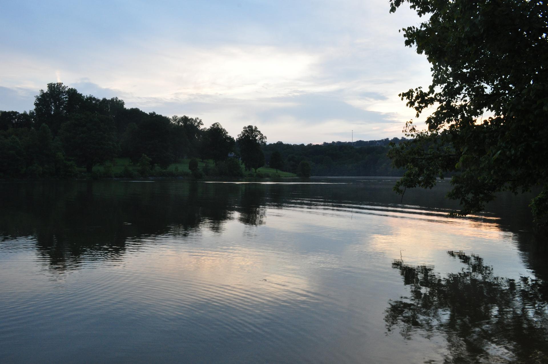 A calm lake reflects a cloudy twilight sky, surrounded by dark trees.