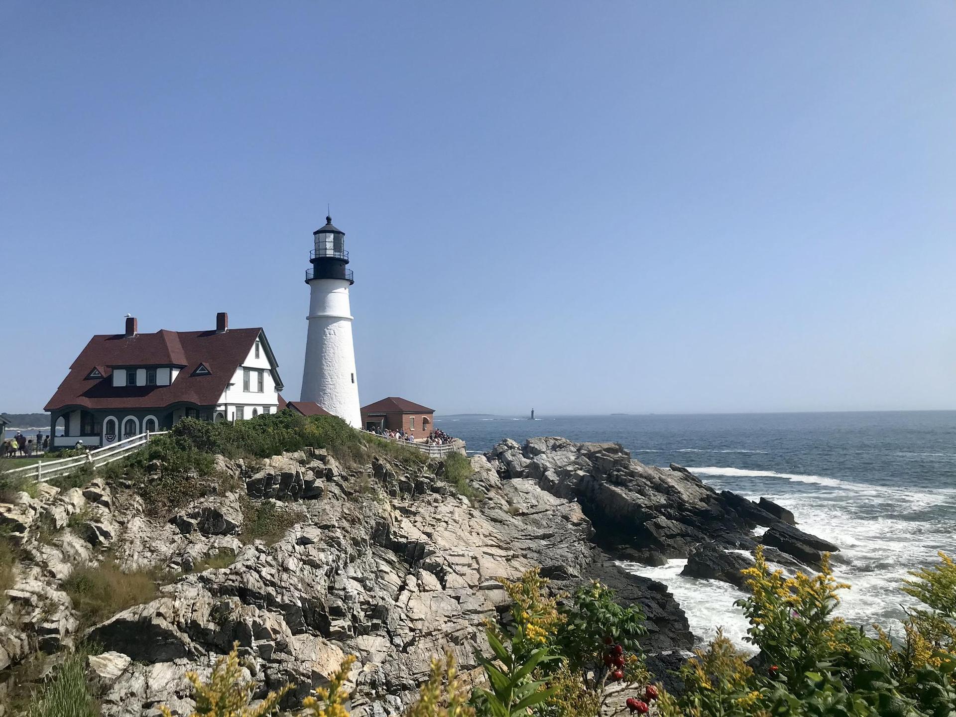 White lighthouse and building on a rocky cliff overlooking the ocean.