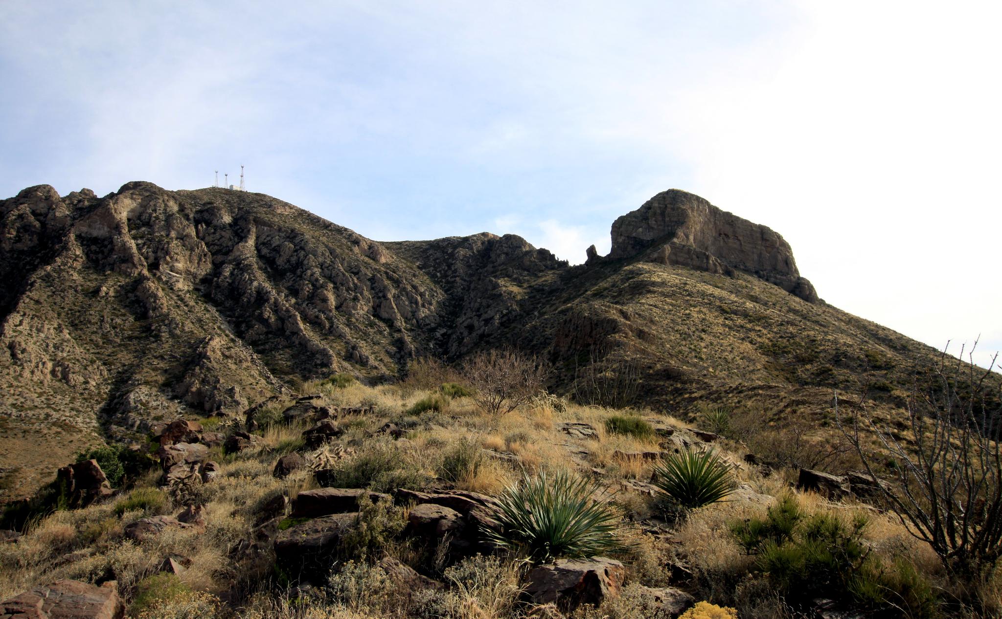 Large rocky mountain with sparse vegetation under a partly cloudy sky.