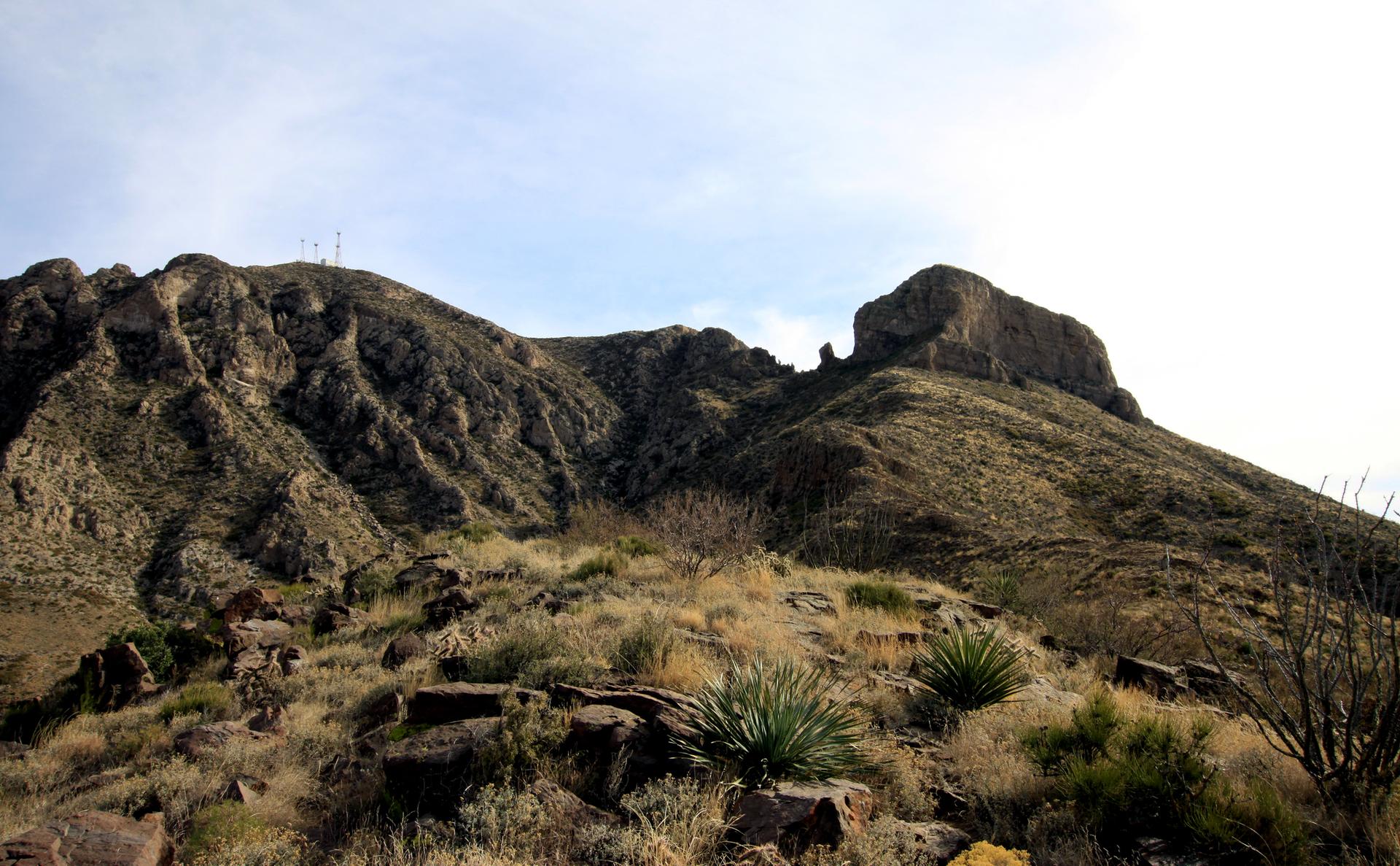 Large rocky mountain with sparse vegetation under a partly cloudy sky.