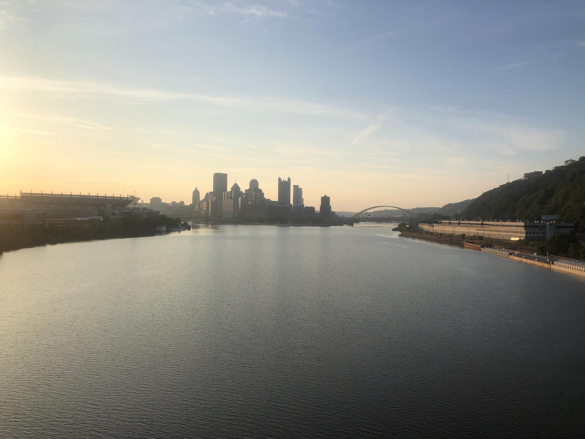 City skyline across a wide river at sunrise, with warm light.