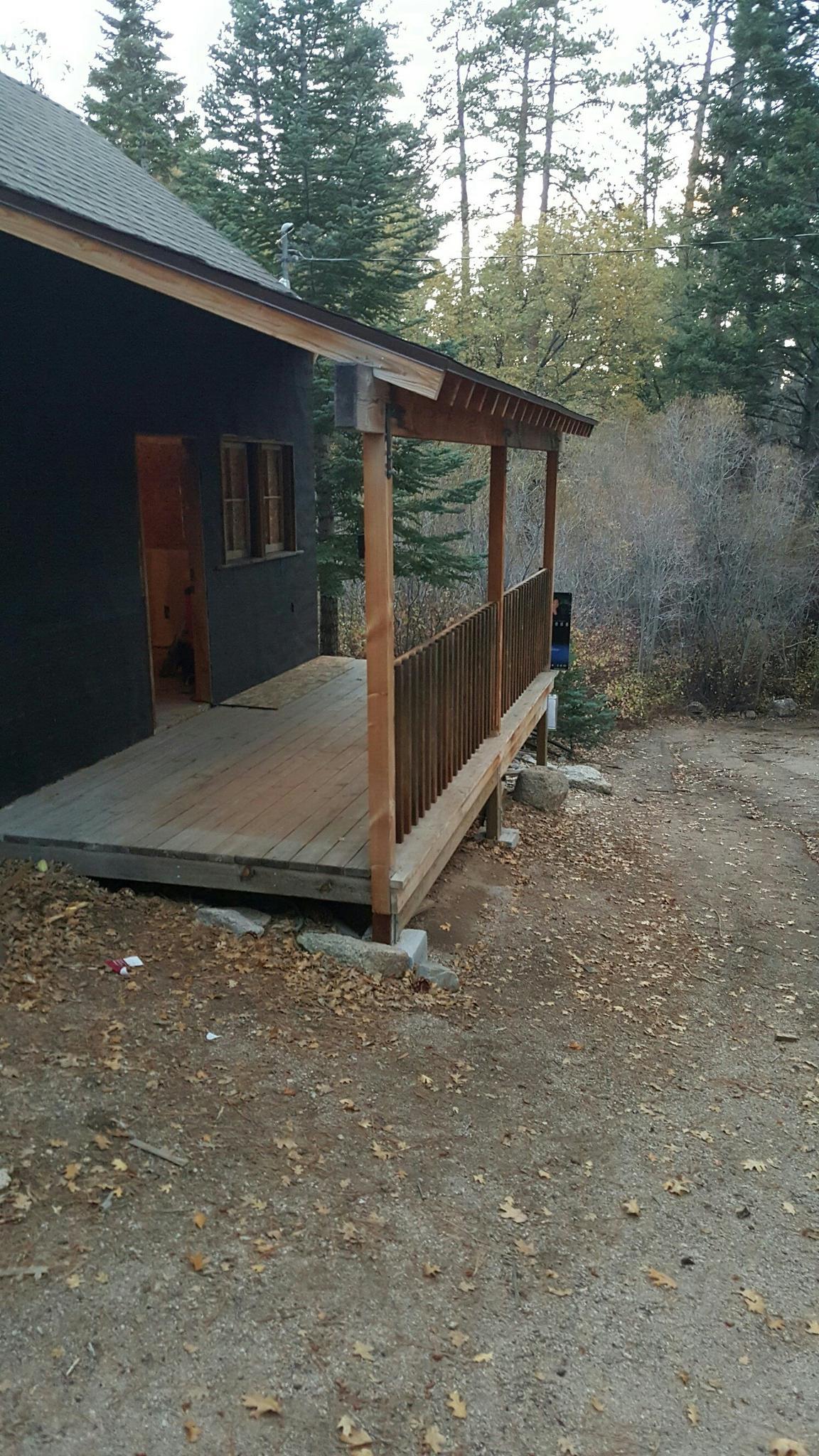 Wooden porch of a dark cabin surrounded by trees and dirt ground.